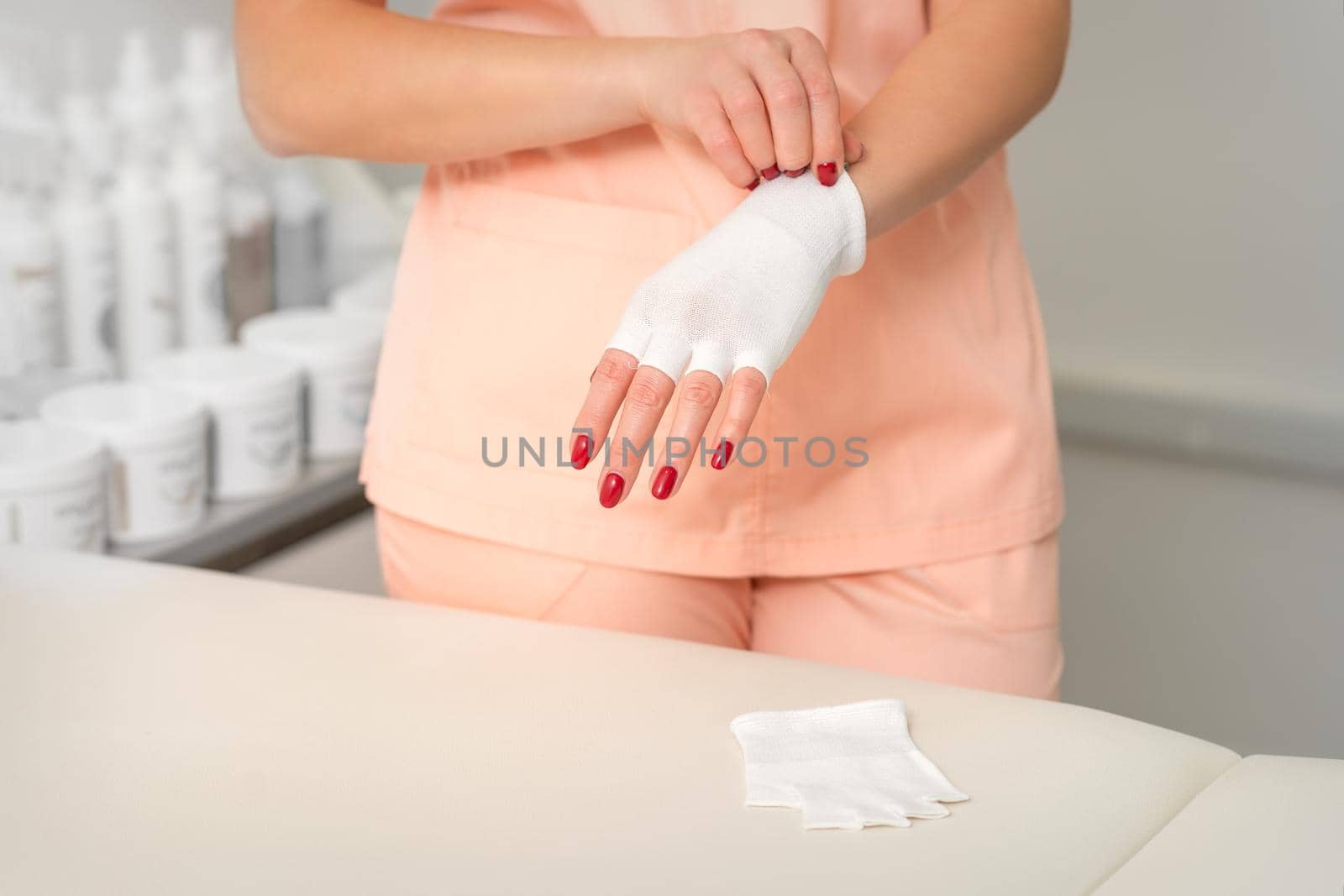 Cosmetologist in workwear wearing white bamboo fingerless gloves on her hands