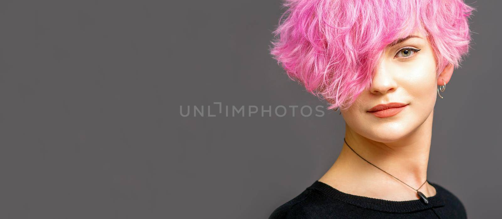 Portrait of beautiful young white woman with a pink short hairstyle on dark background with copy space