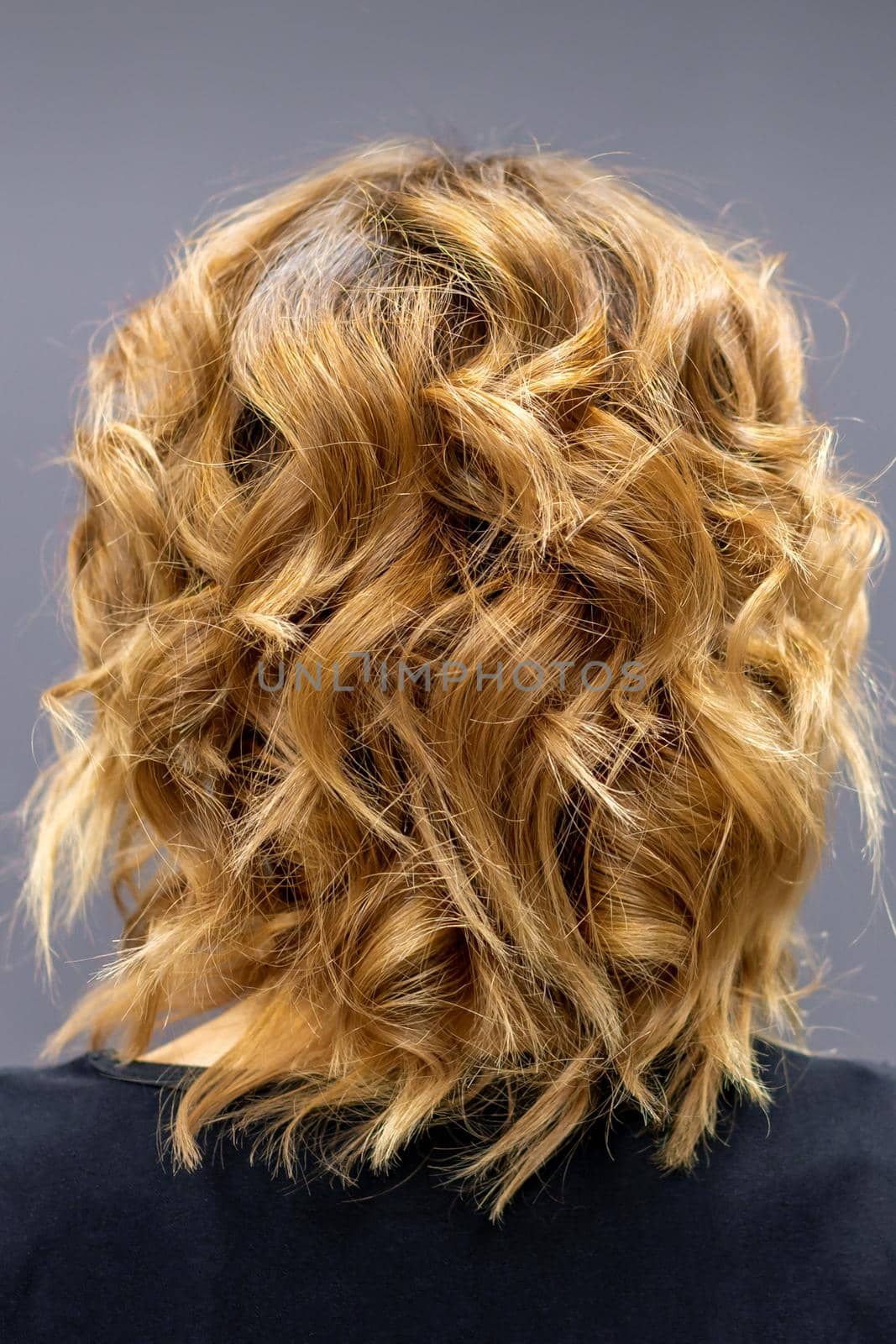 Back view of the woman with long brown curly hair stands on a dark background