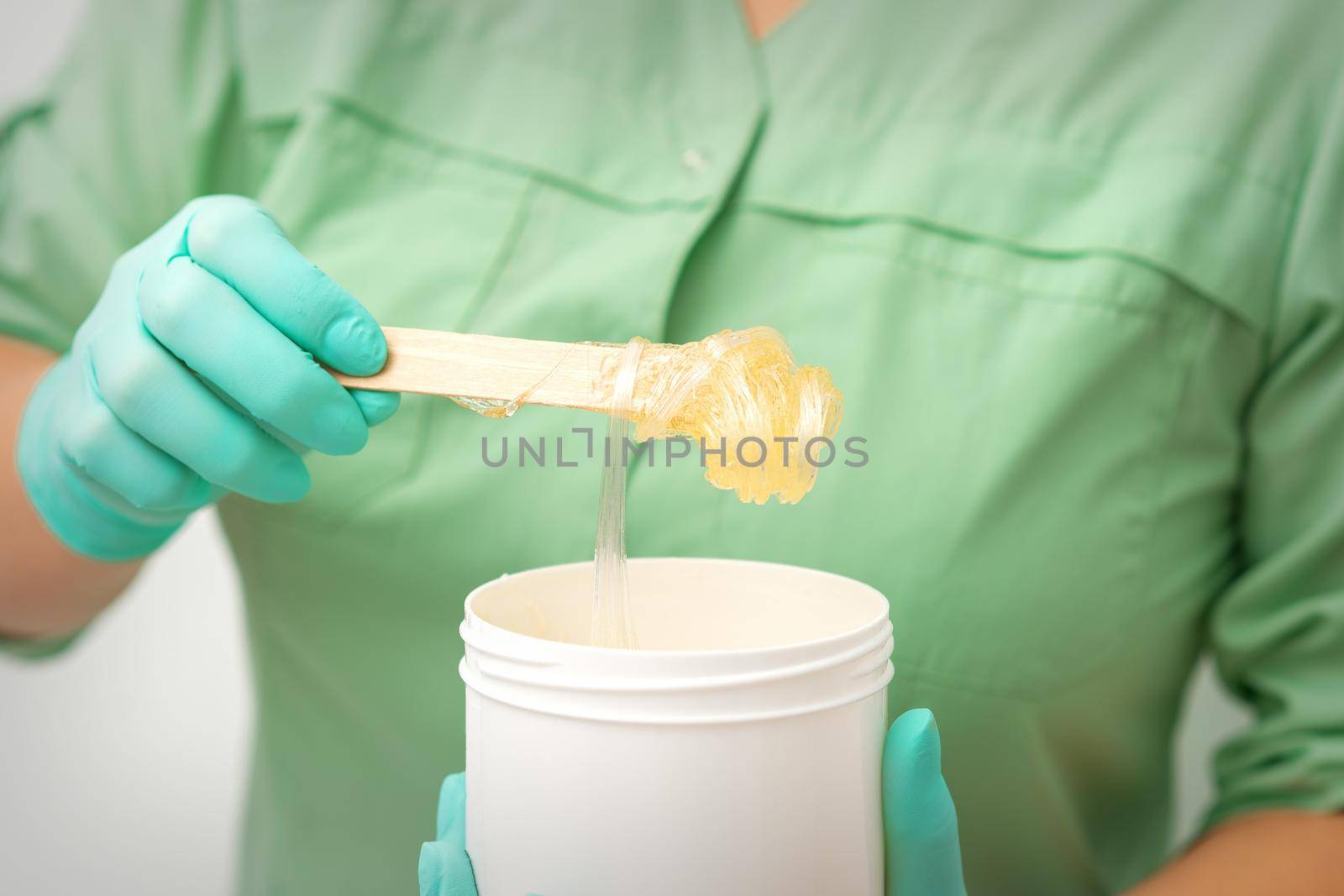 Liquid yellow sugar paste for depilation on a stick flows into the jar in hands of a beautician