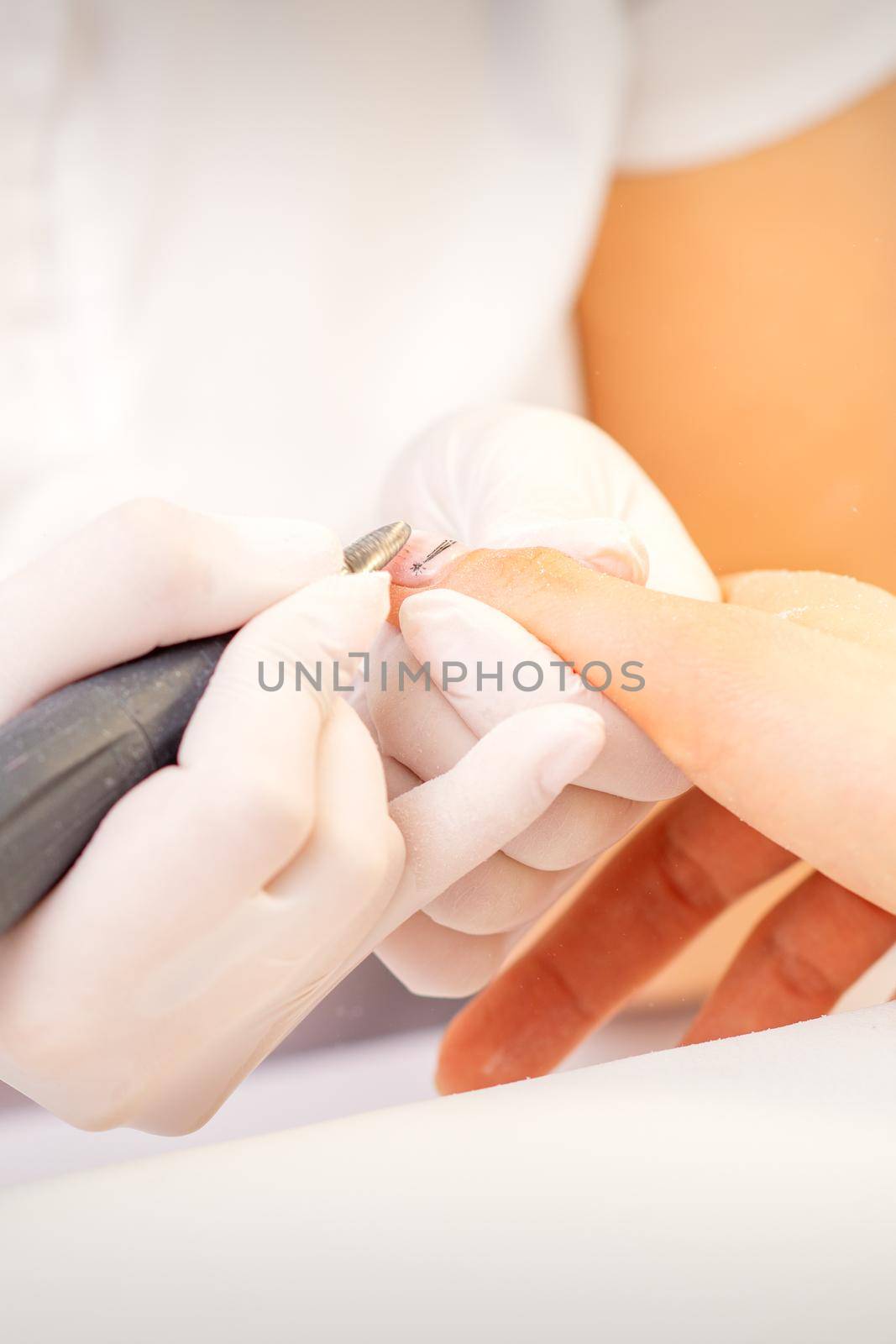 Closeup of manicure master in white gloves applying an electric nail file drill to remove the nail polish in the beauty salon