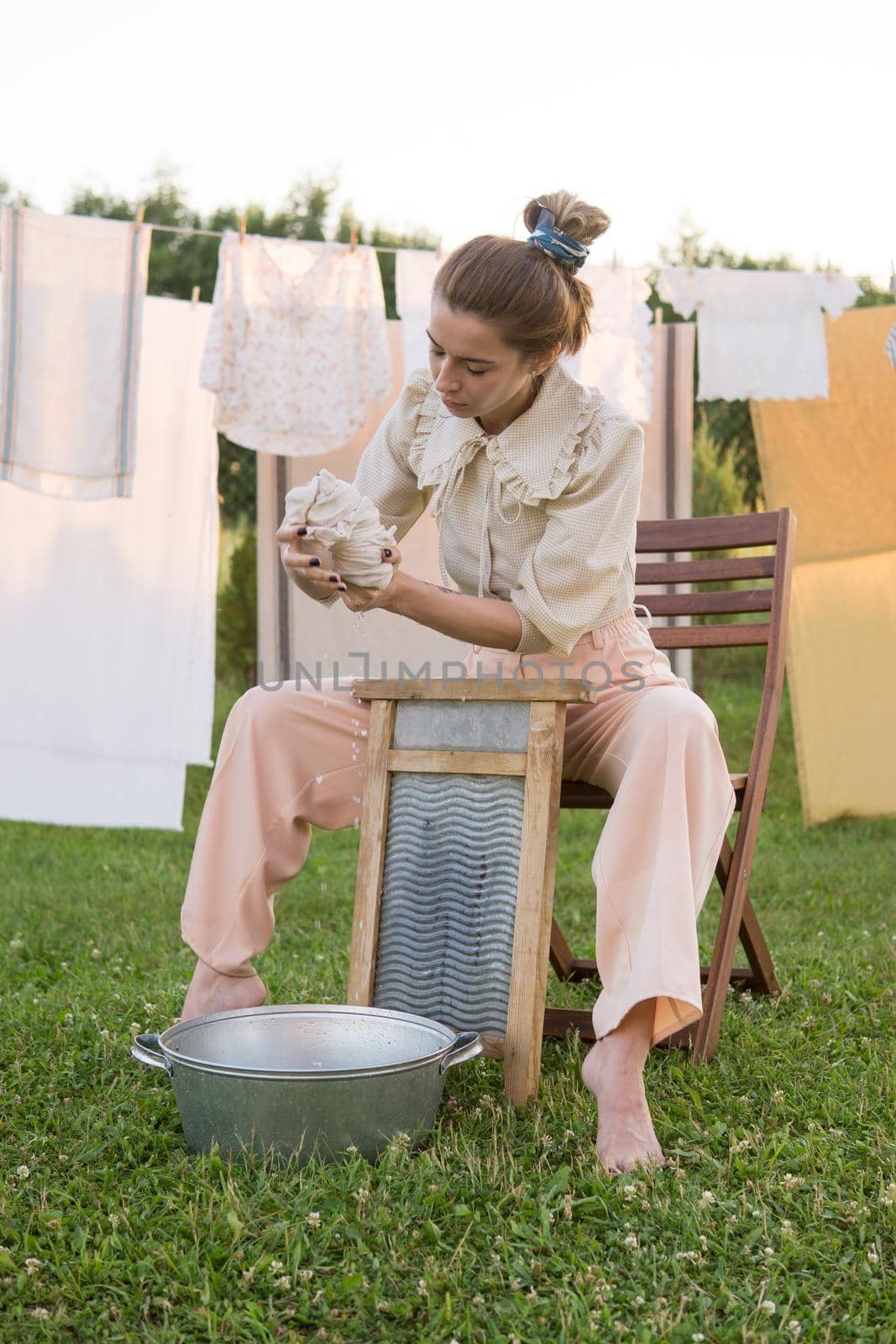Laundry day. A woman hangs linen and towels on a tree in the courtyard of a village house. Summer cottage concept.