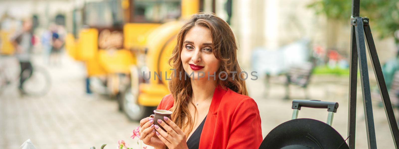 Tourist young caucasian woman in red jacket with coffee cup at the table in cafe outdoors. by okskukuruza