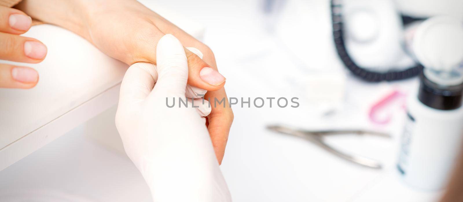 The manicurist holds the female thumb during a manicure procedure in the nail salon. by okskukuruza