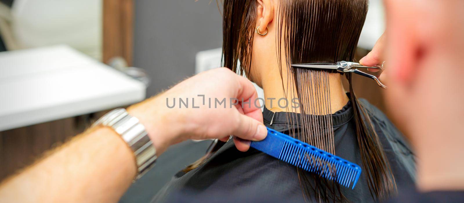 The male hairdresser cuts back female client's hair with scissors and comb in a beauty salon. by okskukuruza
