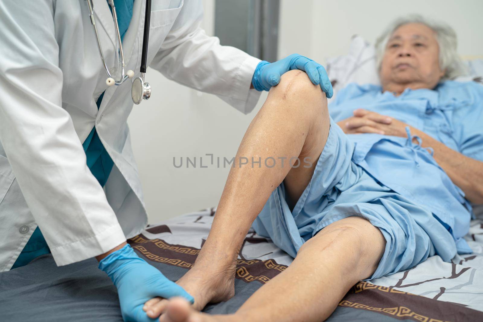 Asian doctor physiotherapist examining, massaging and treatment knee and leg of senior patient in orthopedist medical clinic nurse hospital. by pamai