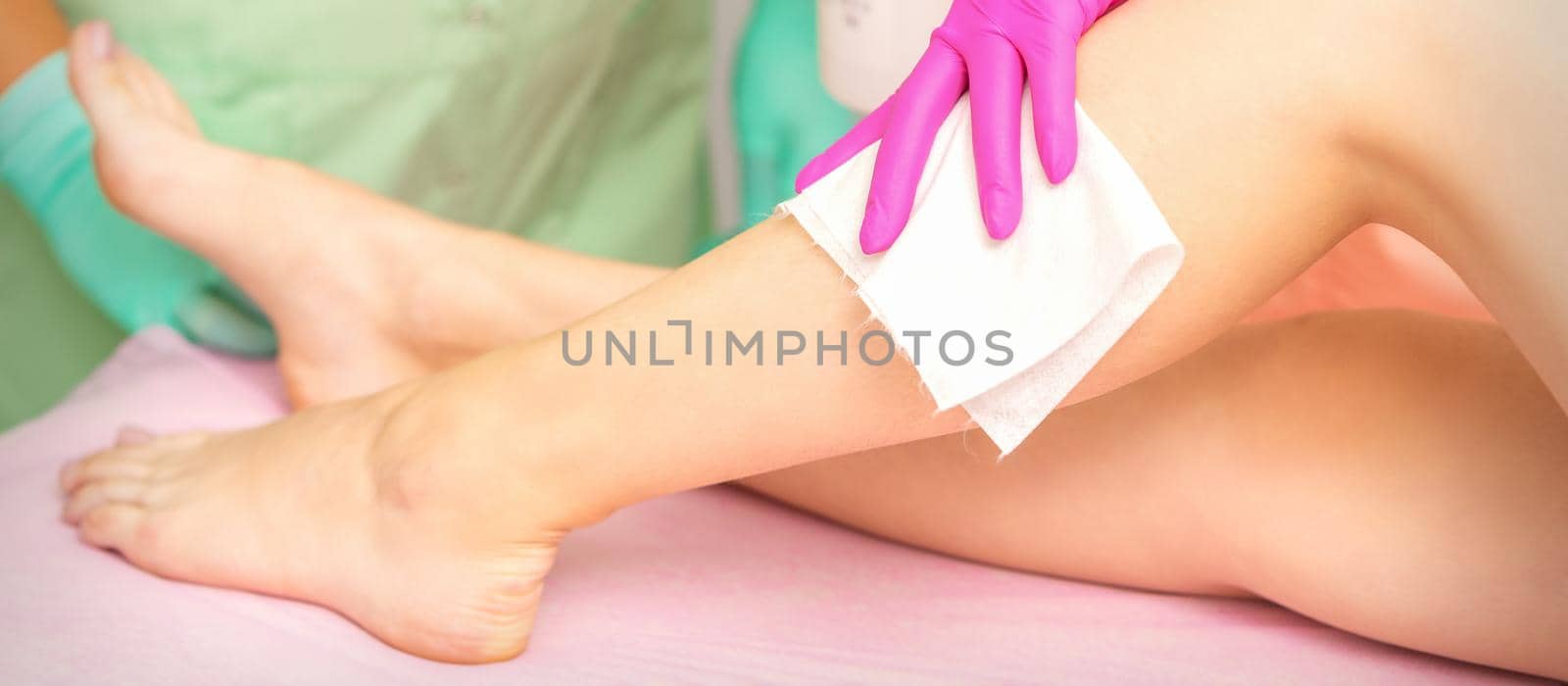 Master of depilation wipes female feet with white napkin preparing for the procedure of hair removal