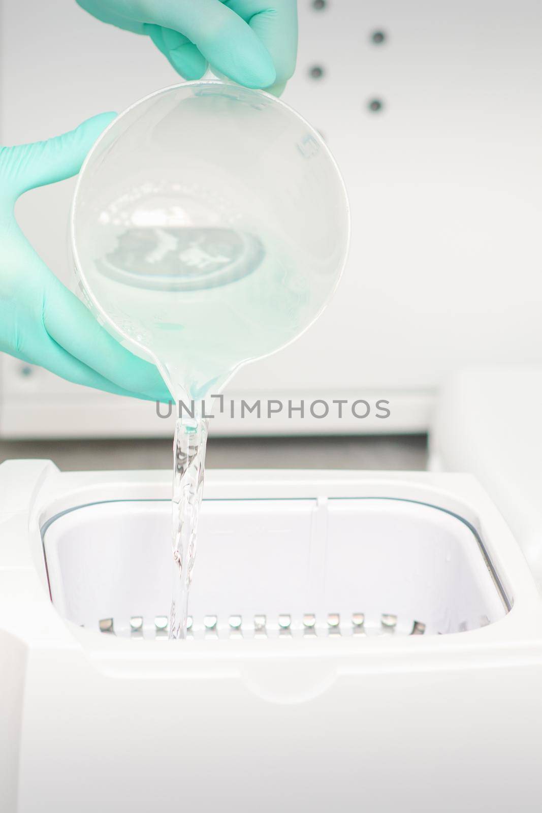 The beautician adds liquid for disinfection of instruments to the machine for sterilization of tools