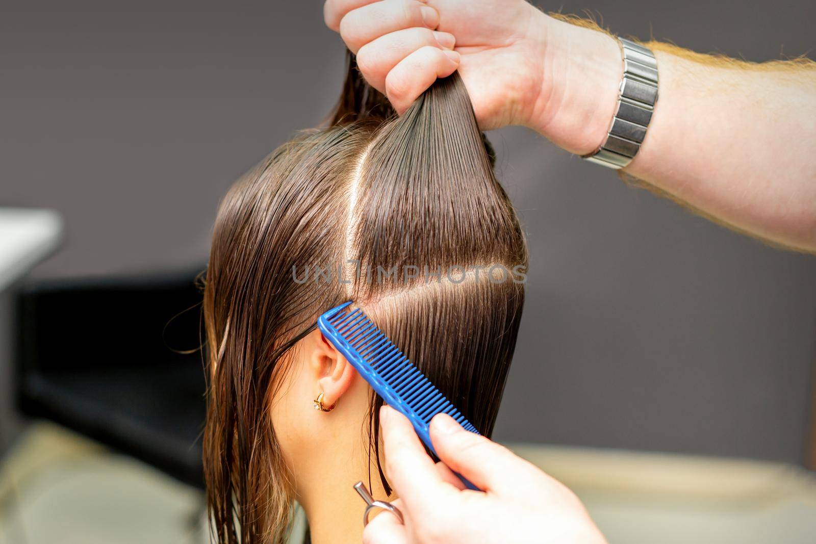 Male coiffeur divides women hair into sections with comb and hands in a beauty salon