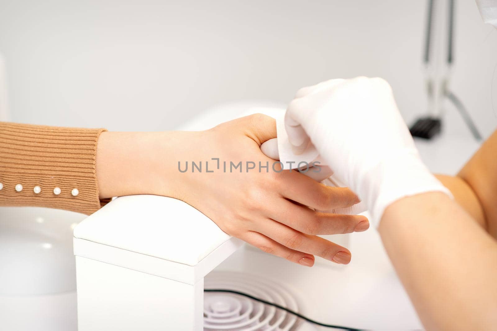 Hands of a manicurist in white protective gloves wipe female nails with a paper napkin in the salon. by okskukuruza