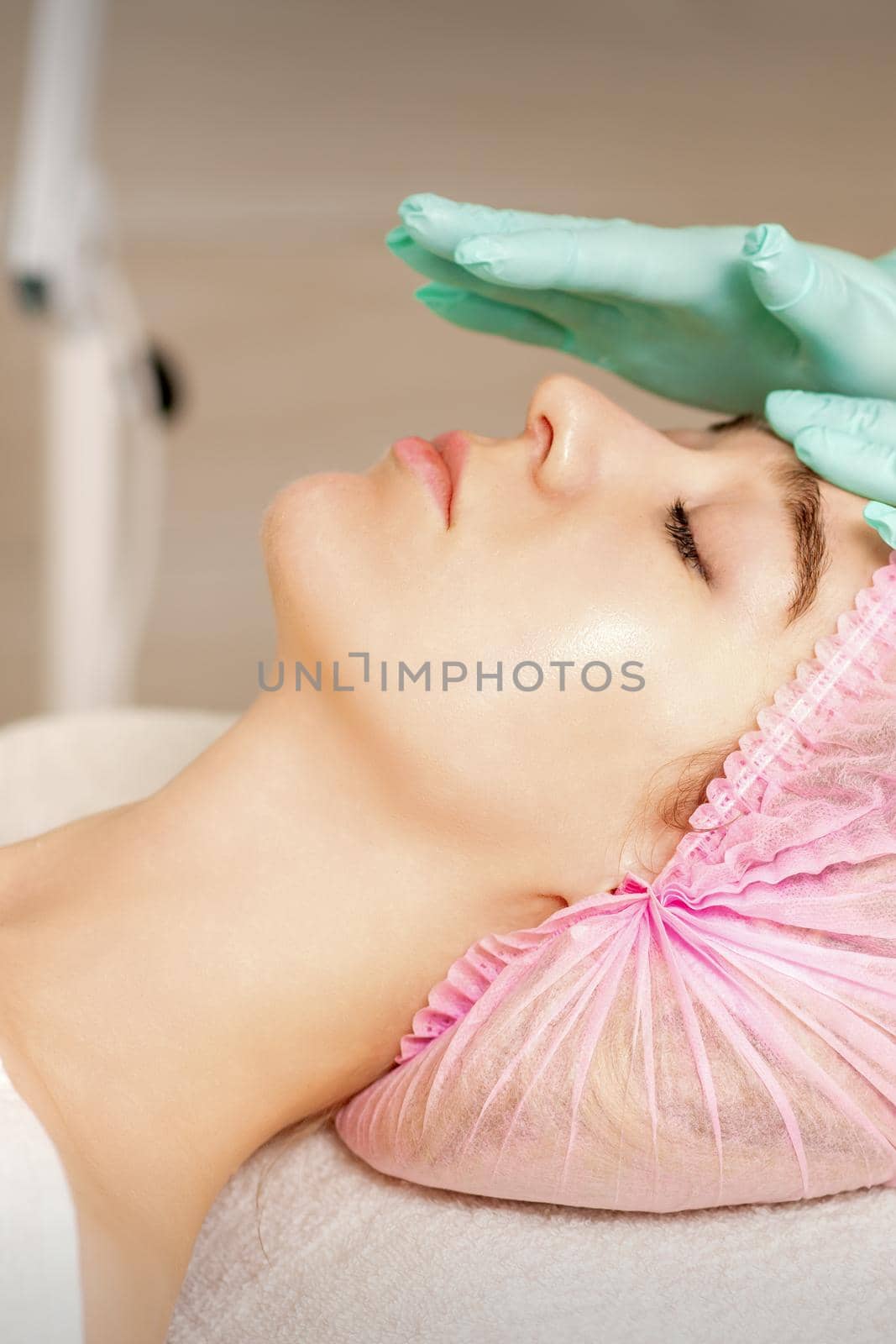 The woman is having cosmetic treatment during cosmetologist in medical gloves are touching the female face at the spa salon. by okskukuruza