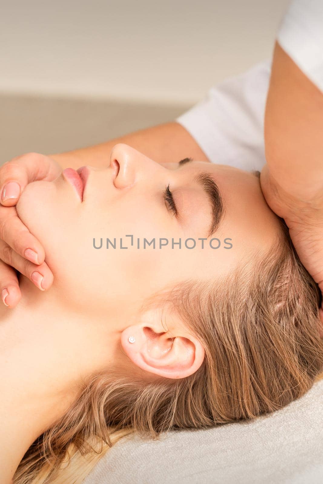 Cosmetologist hands doing facial massage on forehead and chin of young female at spa salon