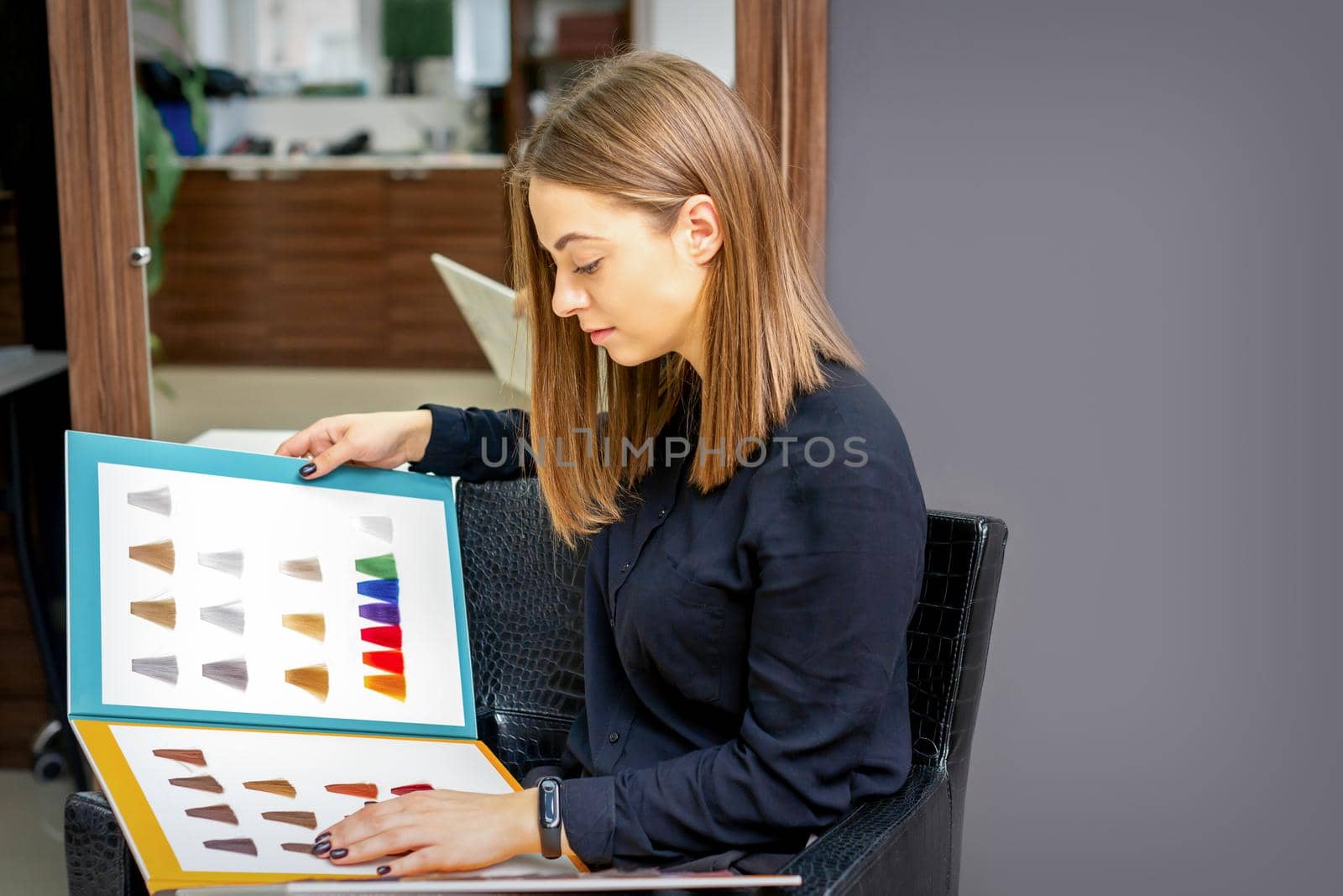 Young caucasian woman choosing a color from the hair color chart in a beauty salon