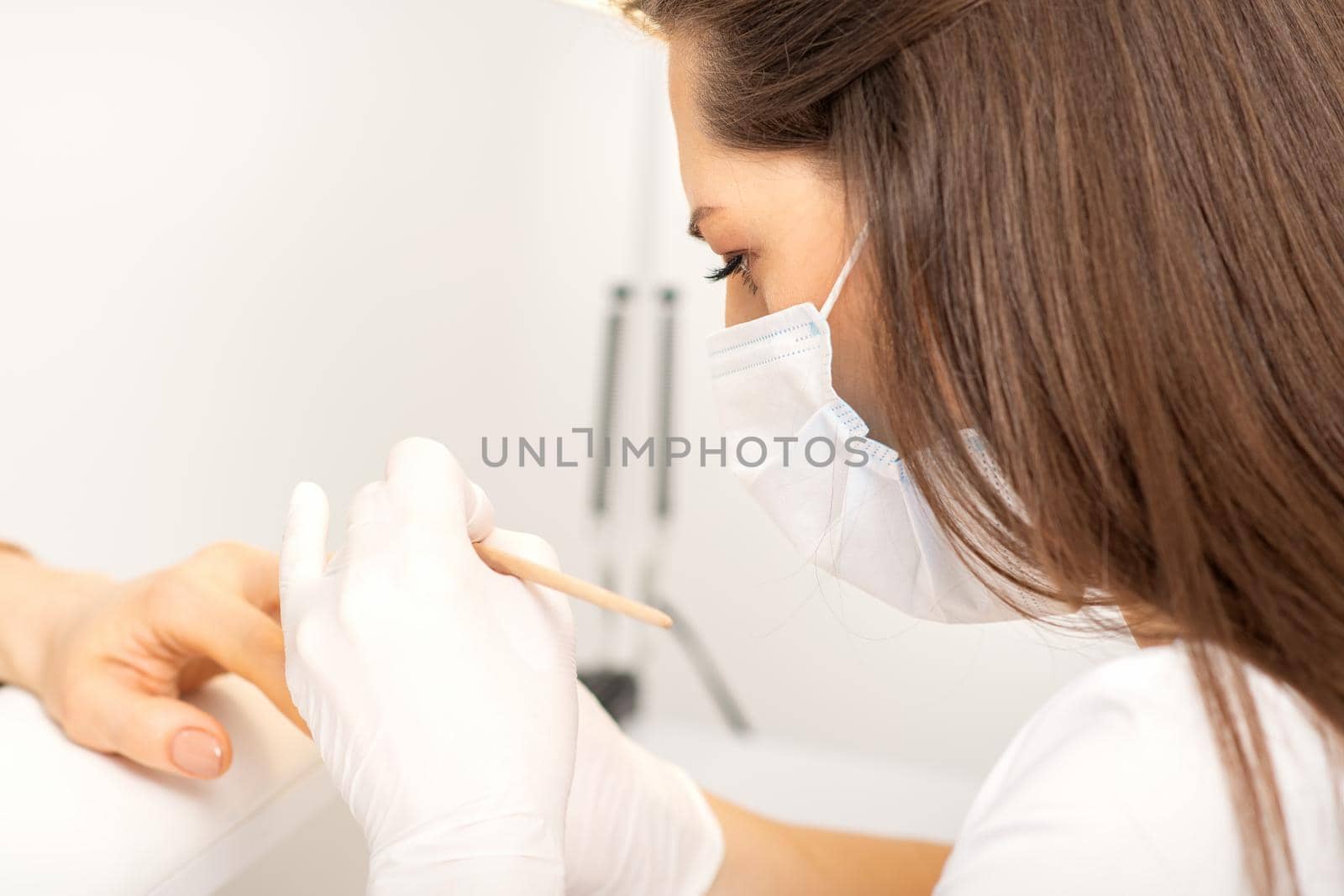 Manicure master in protective face mask and white gloves apply polish to female fingernails. by okskukuruza