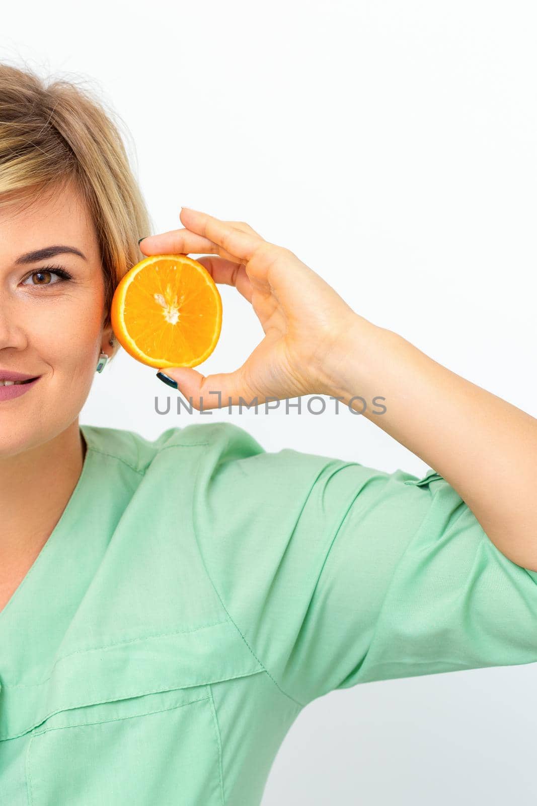 Portrait of young smiling blonde woman cosmetologist with halves of oranges on white background