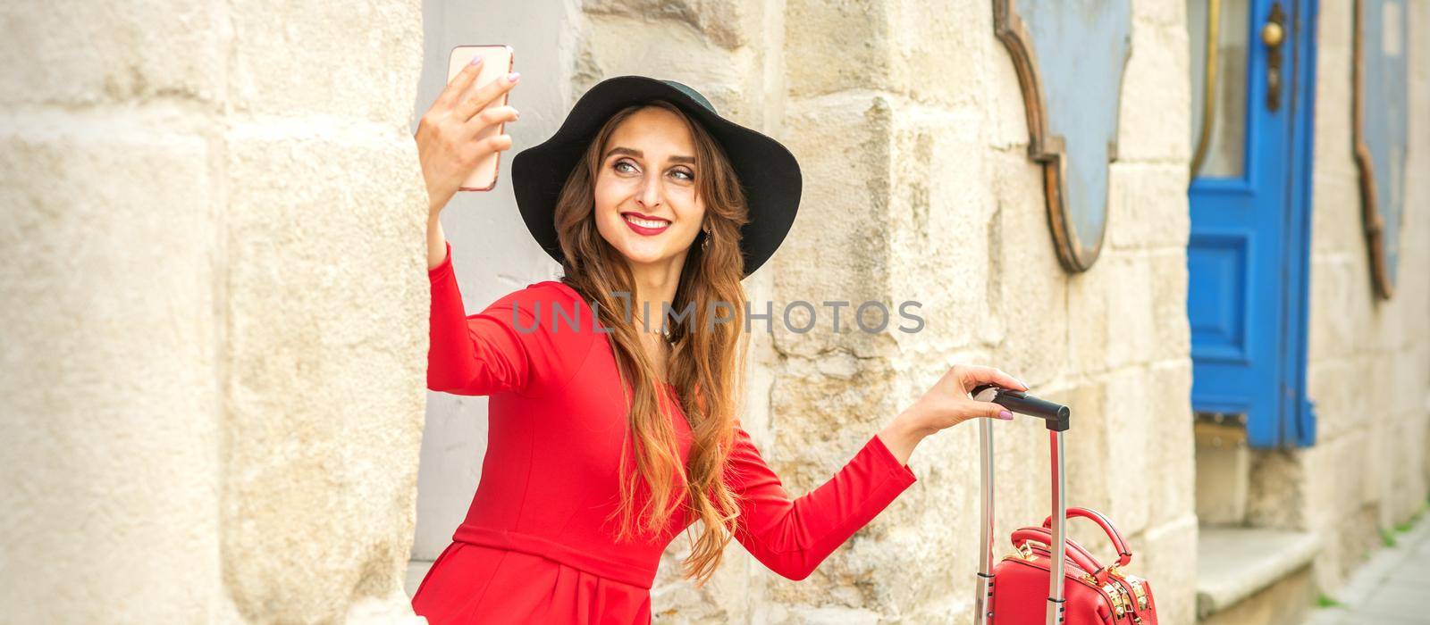 Beautiful young caucasian woman in black hat looking on the smartphone smiling and sitting on stairs at the door outdoors. by okskukuruza