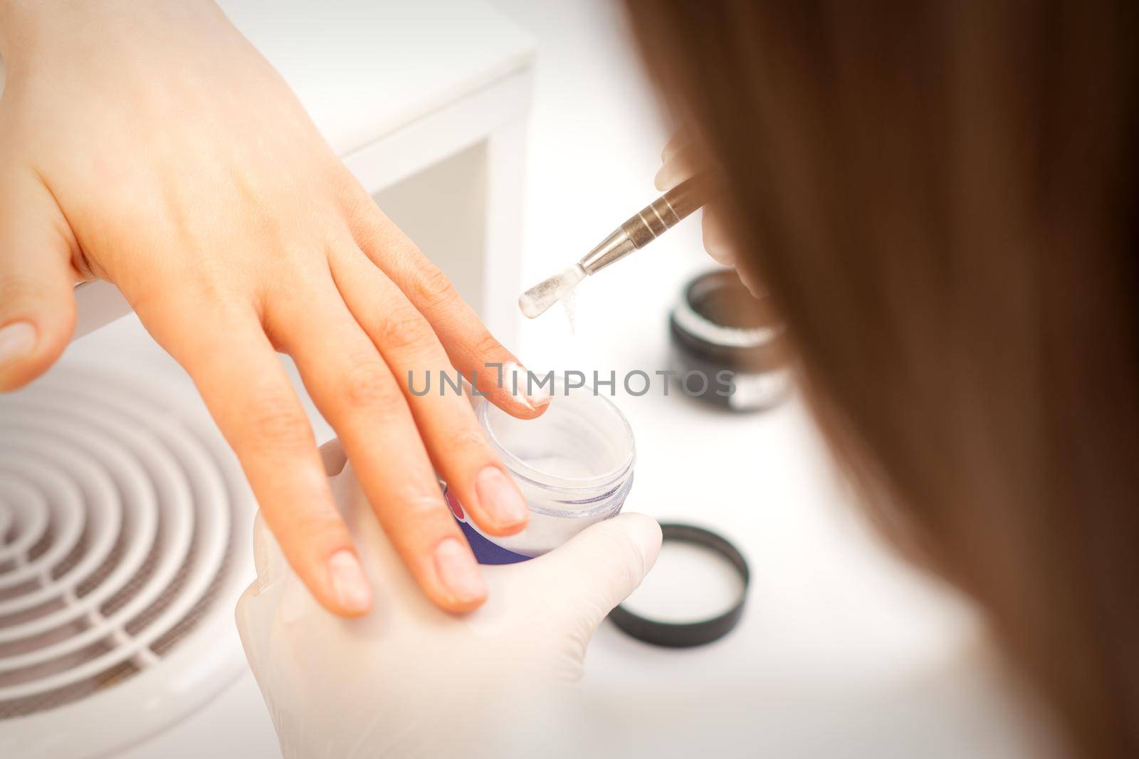 Manicure master applying acrylic powder on the female nails in a beauty salon. Strengthening of nails acrylic powder