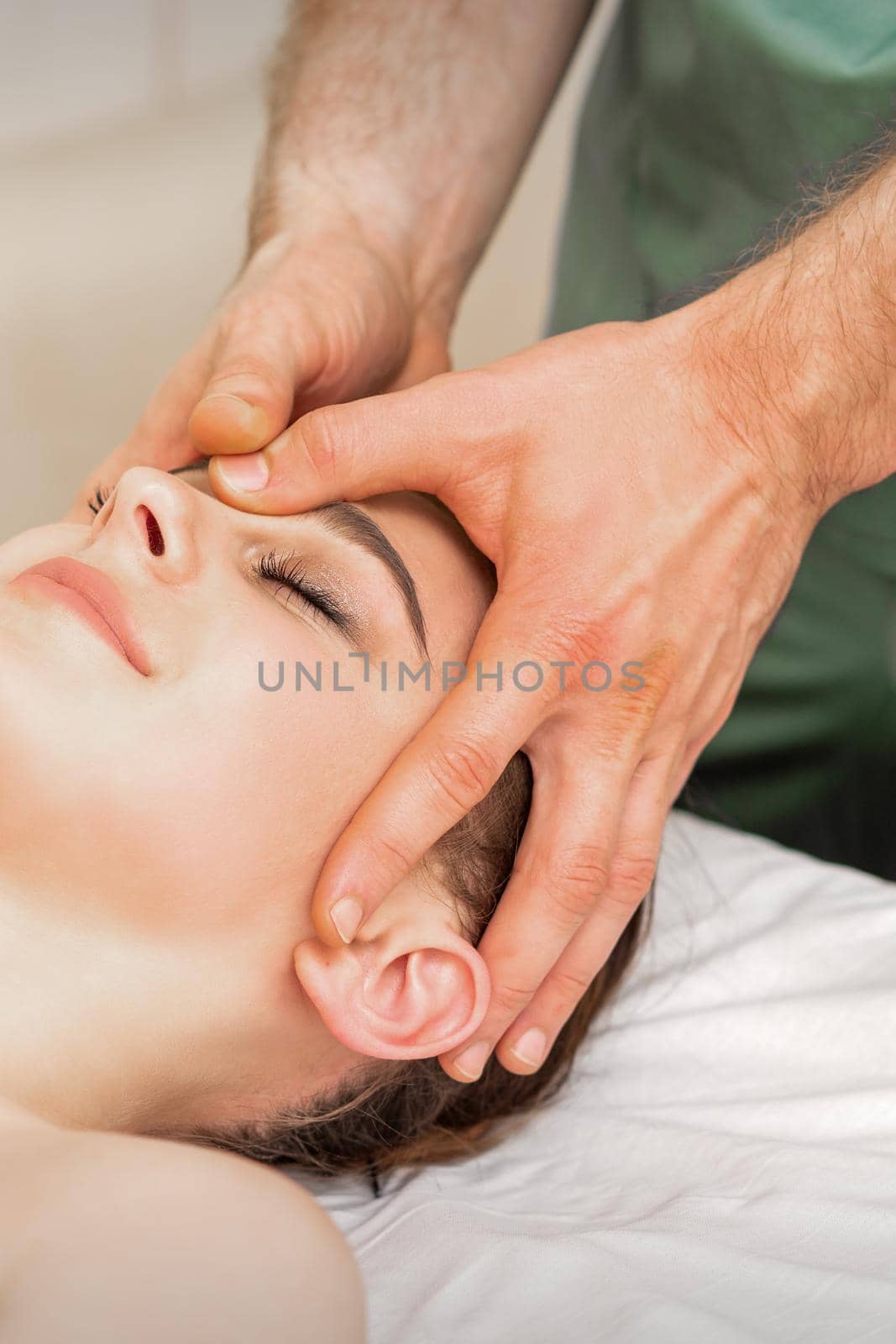 Pretty young caucasian woman receiving a head massage by a male massage therapist in a beauty salon. by okskukuruza