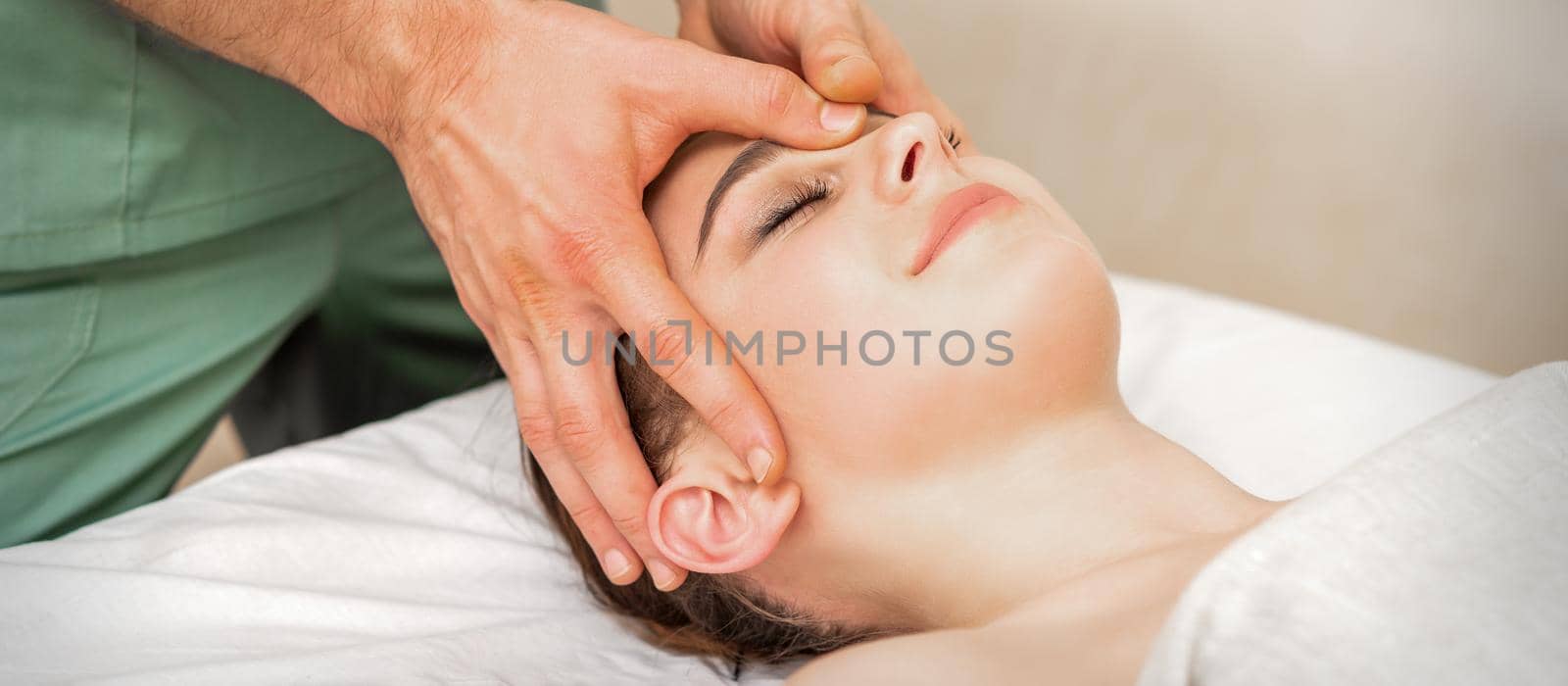 Pretty young caucasian woman receiving a head massage by a male massage therapist in a beauty salon. by okskukuruza