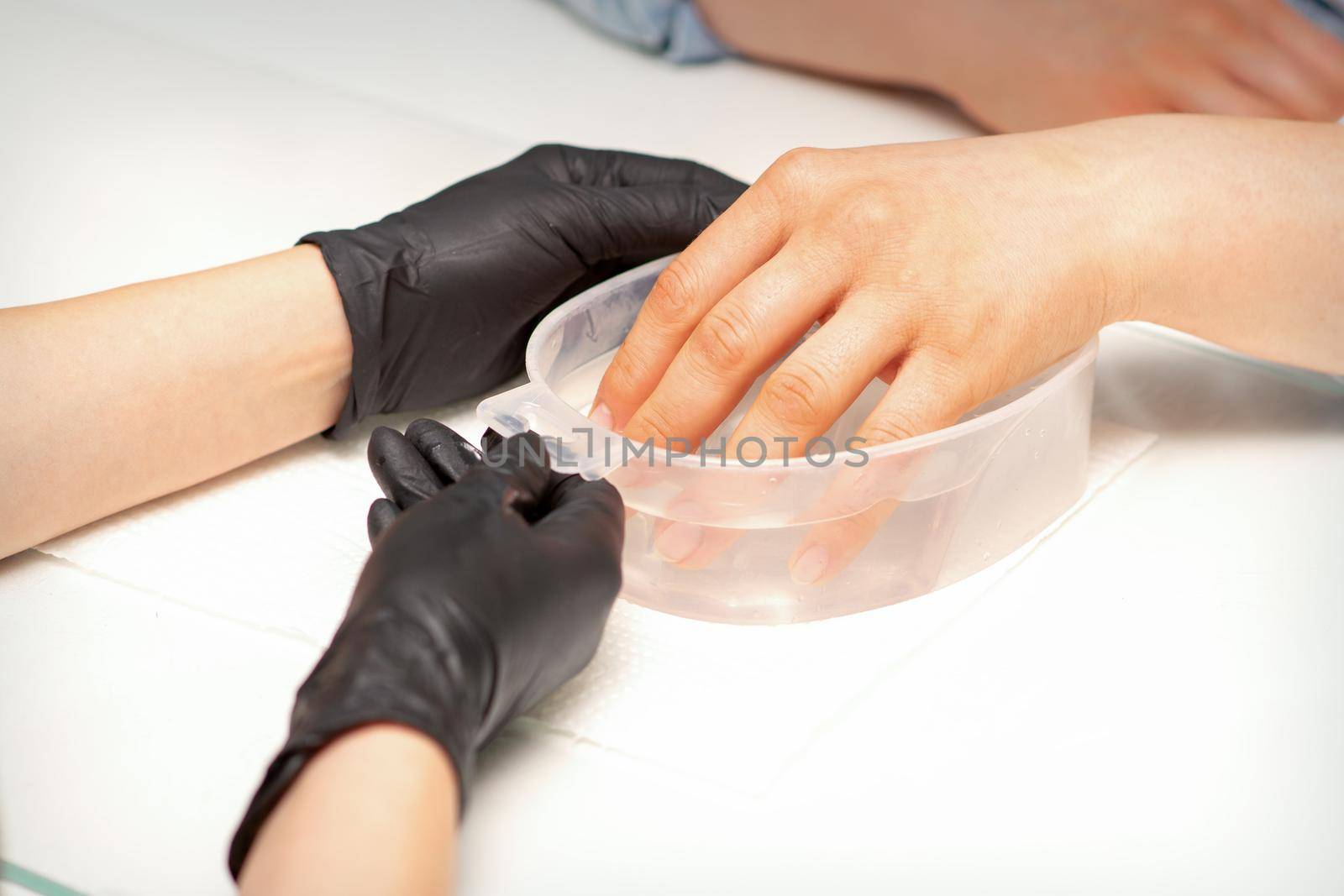 The female dipped her hand in a bowl of water softening nails preparing for the manicure