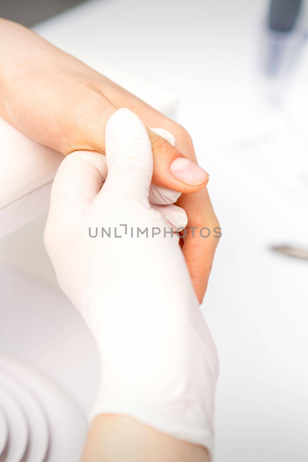 The manicurist holds the female thumb during a manicure procedure in the nail salon