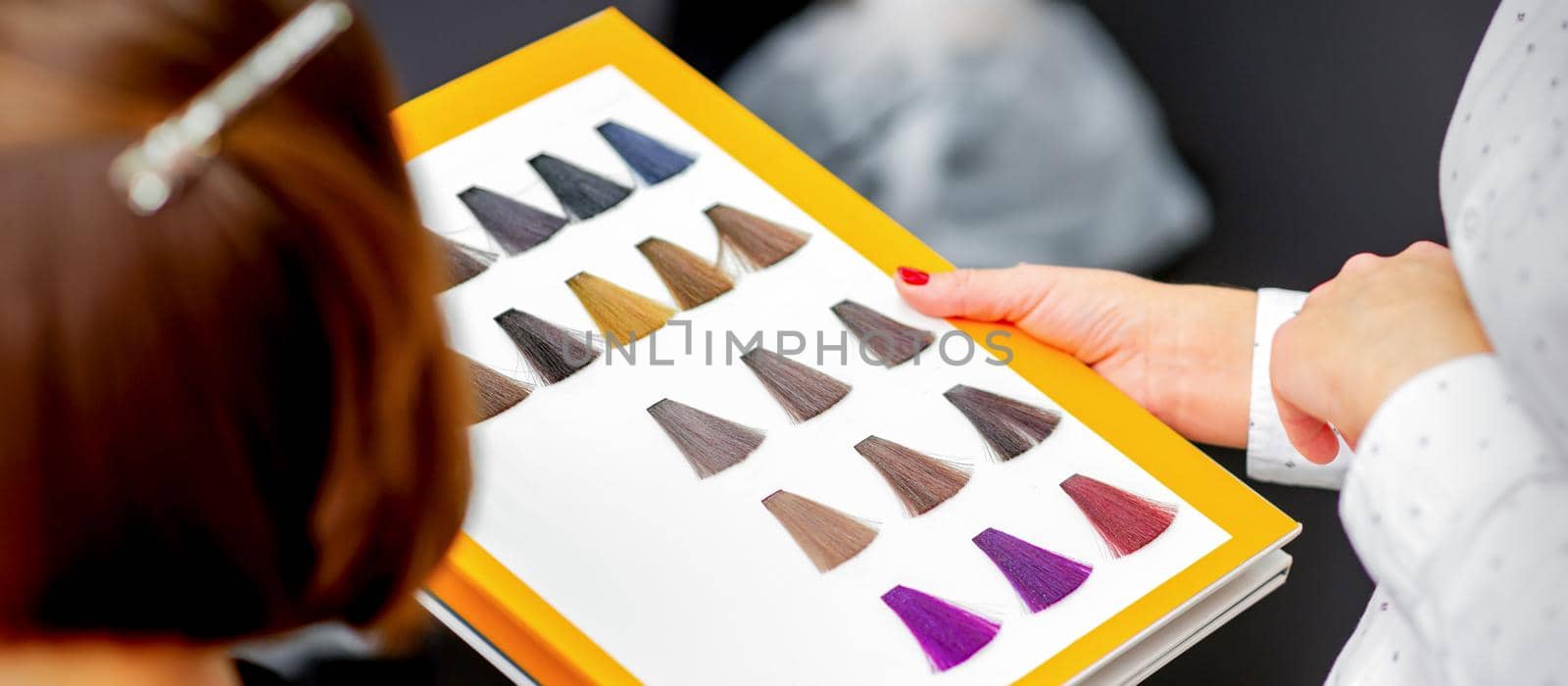 Young caucasian woman choosing a color from the hair color chart in a beauty salon. by okskukuruza