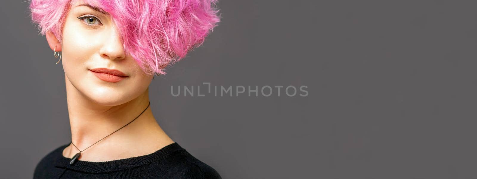 Portrait of beautiful young white woman with a pink short hairstyle on dark background with copy space