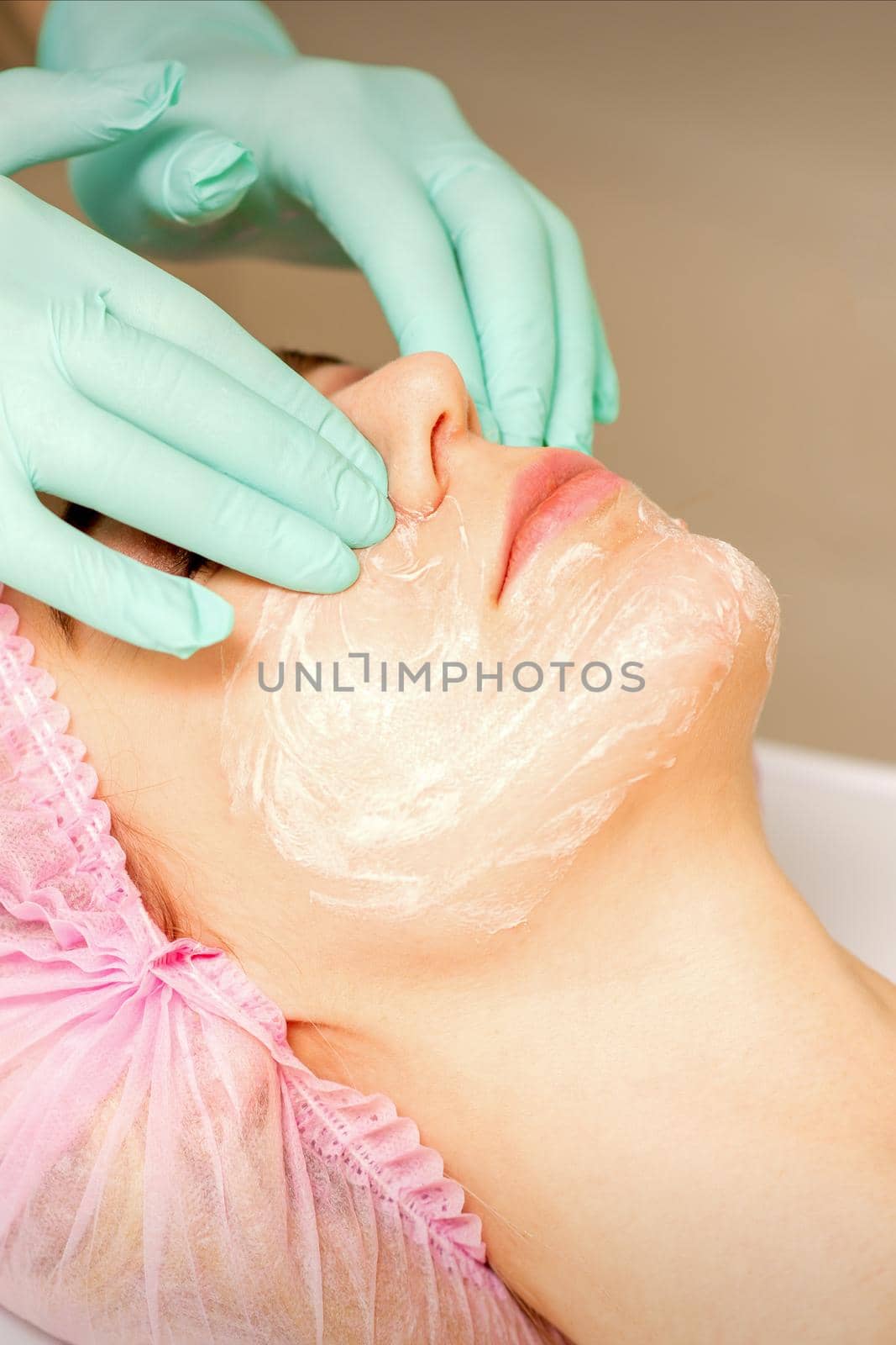 A cosmetologist is applying cream on the female face, close-up view. Woman with doctor beautician in beauty clinic