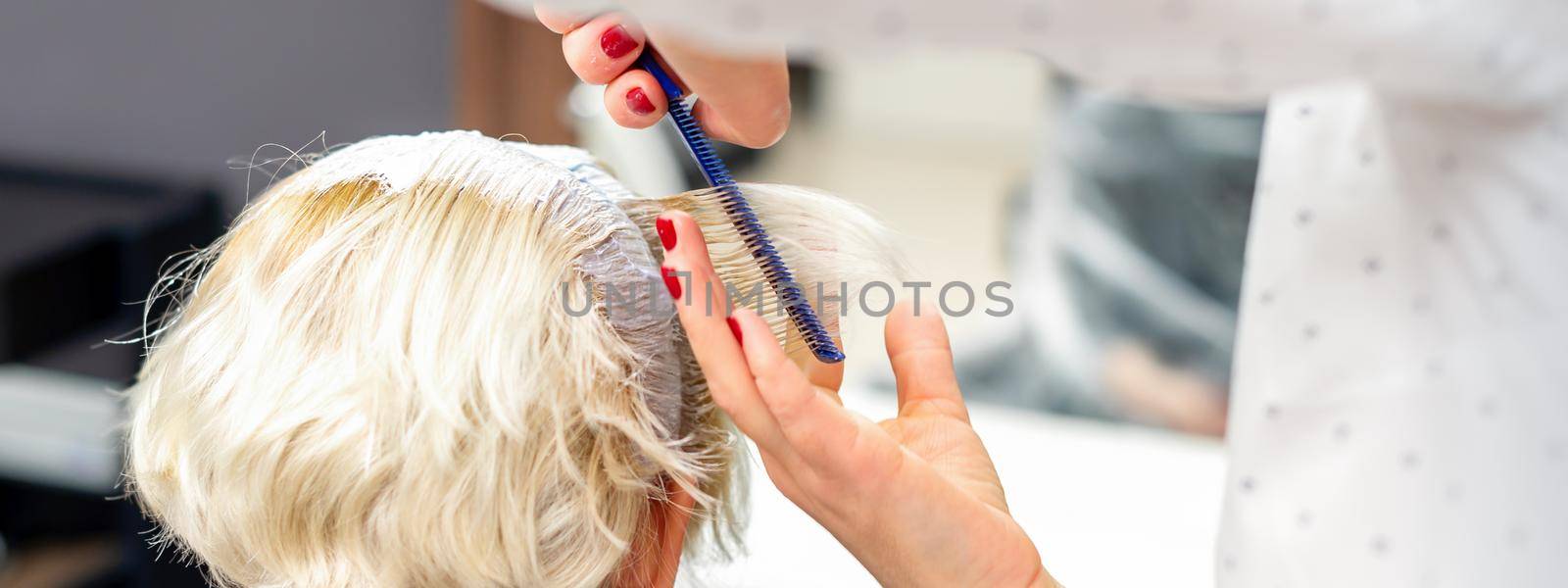 Female hairdresser styling short white hair of the young blonde woman with hands and comb in a hair salon