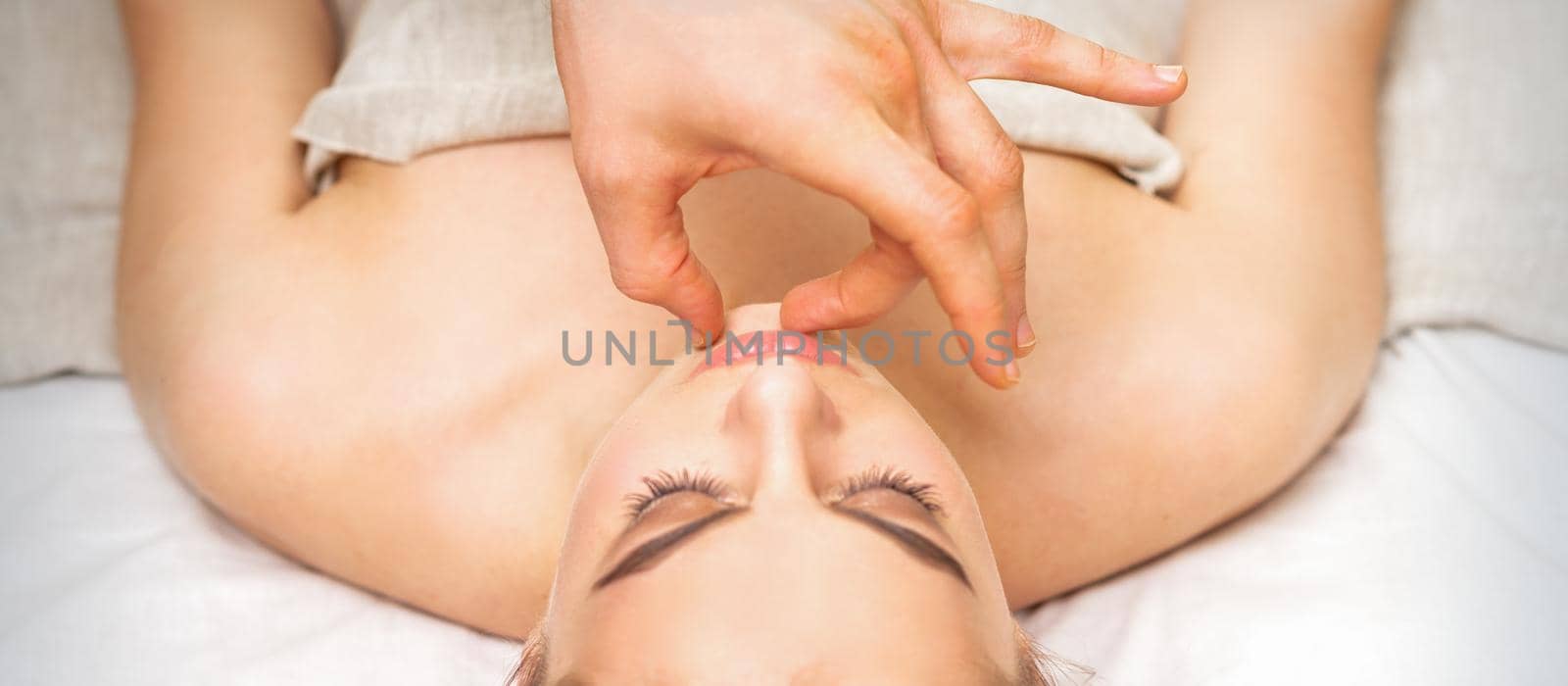 Young caucasian woman receiving chin massage by male therapist fingers in spa salon