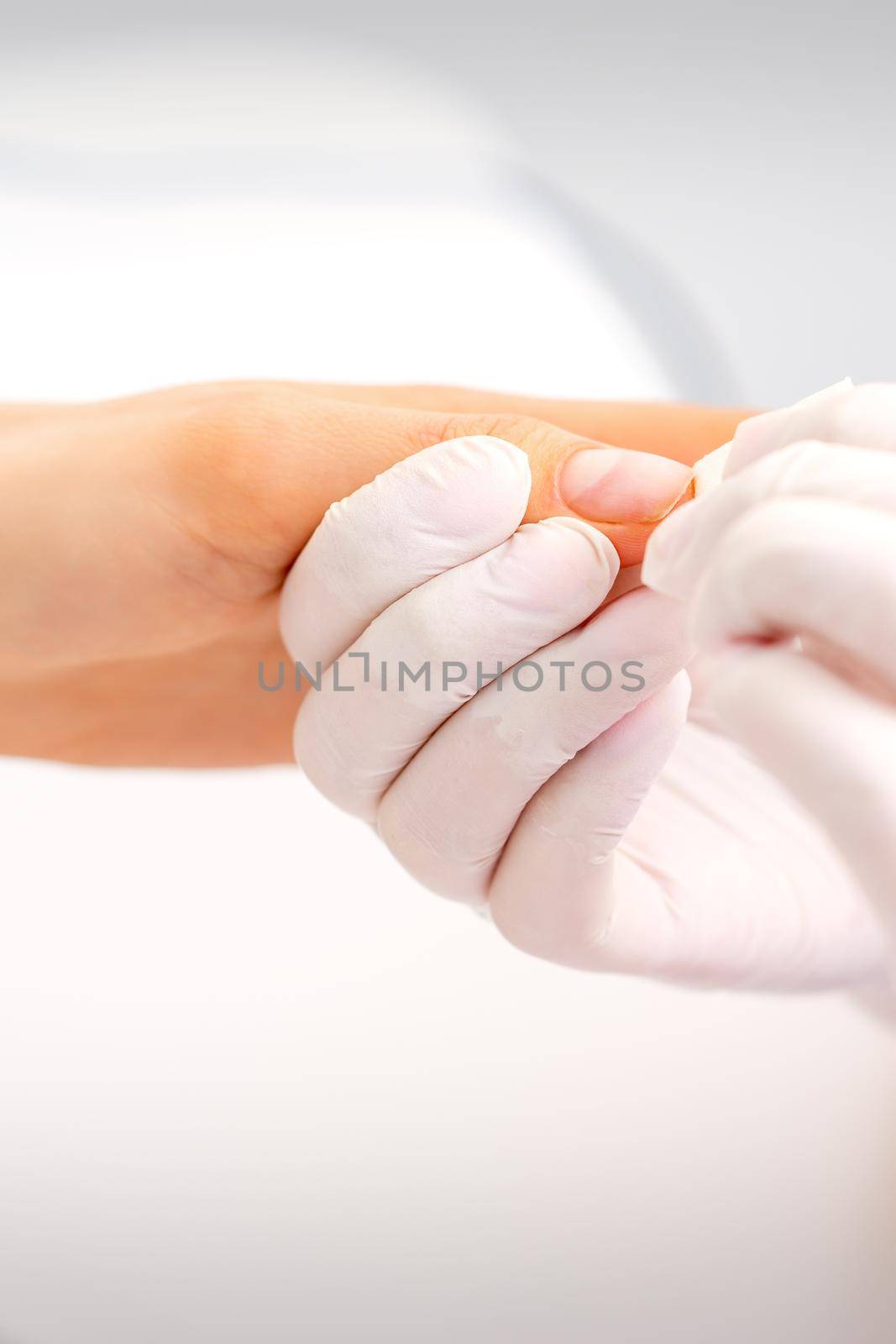 Manicure master wiping the moisturizer from the end of female fingers in beauty salon