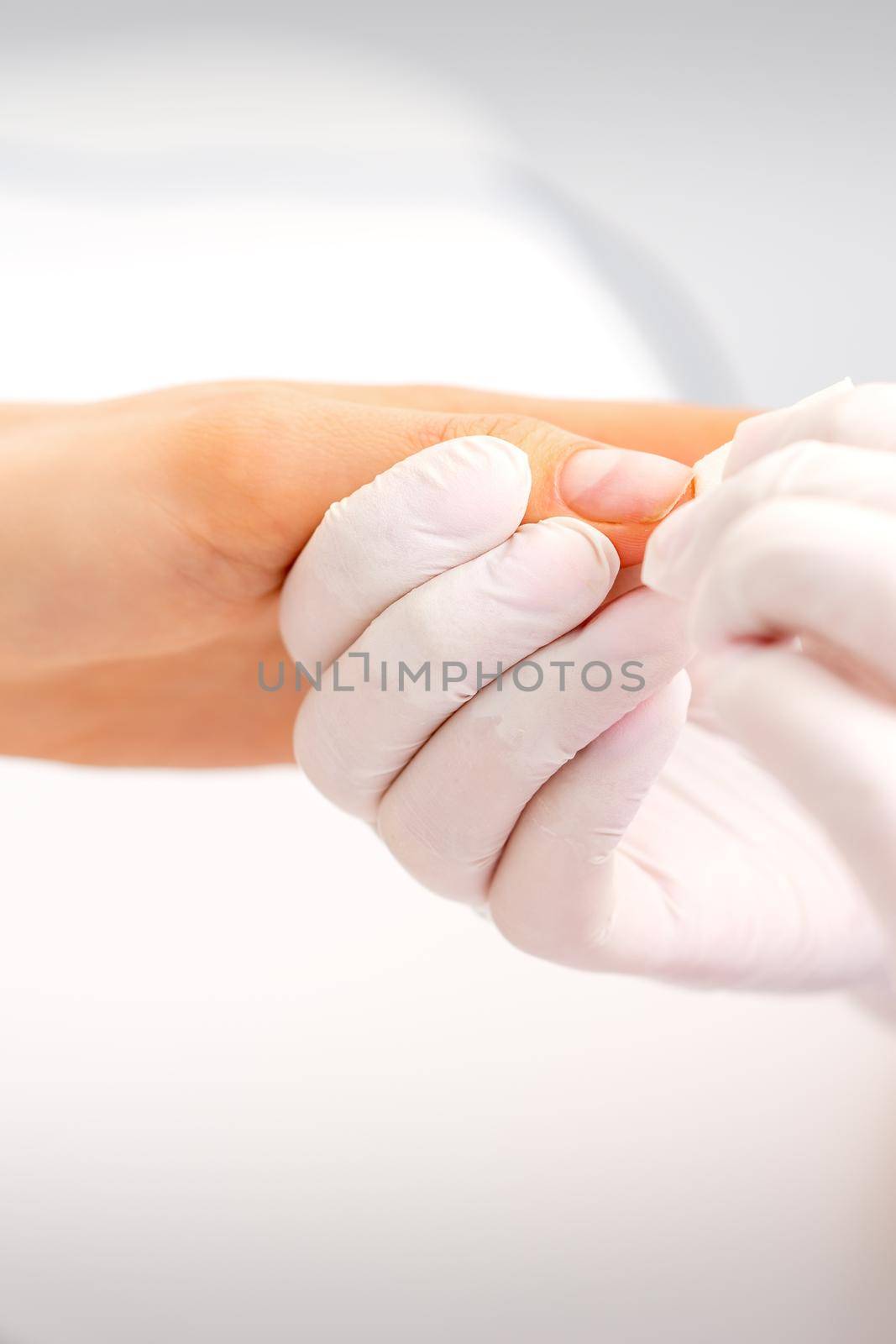 Manicure master wiping the moisturizer from the end of female fingers in beauty salon. by okskukuruza