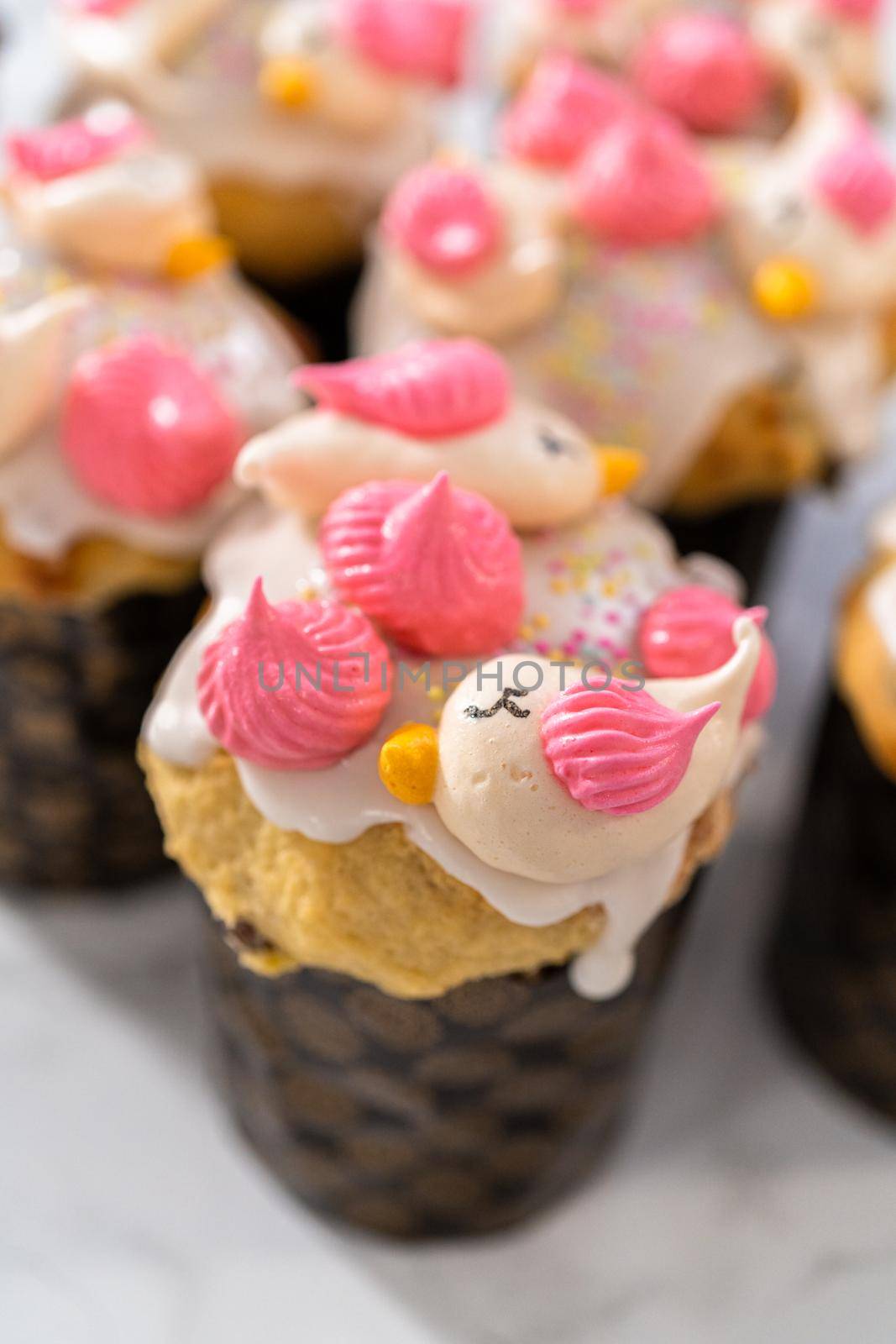 Freshly baked mini Easter bread kulich with lemon glaze, decorated with sprinkles and meringue bird-shaped cookies.