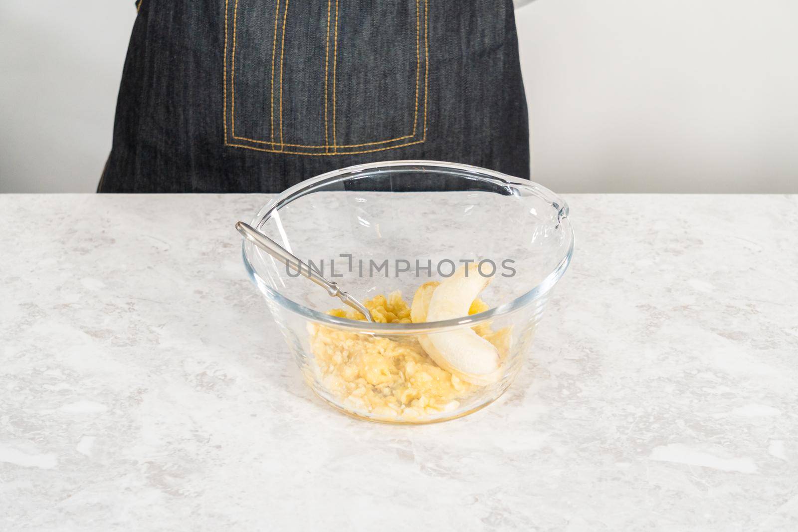 Smashing riped bananas in a glass mixing bowl to prepare coconut banana pancakes.