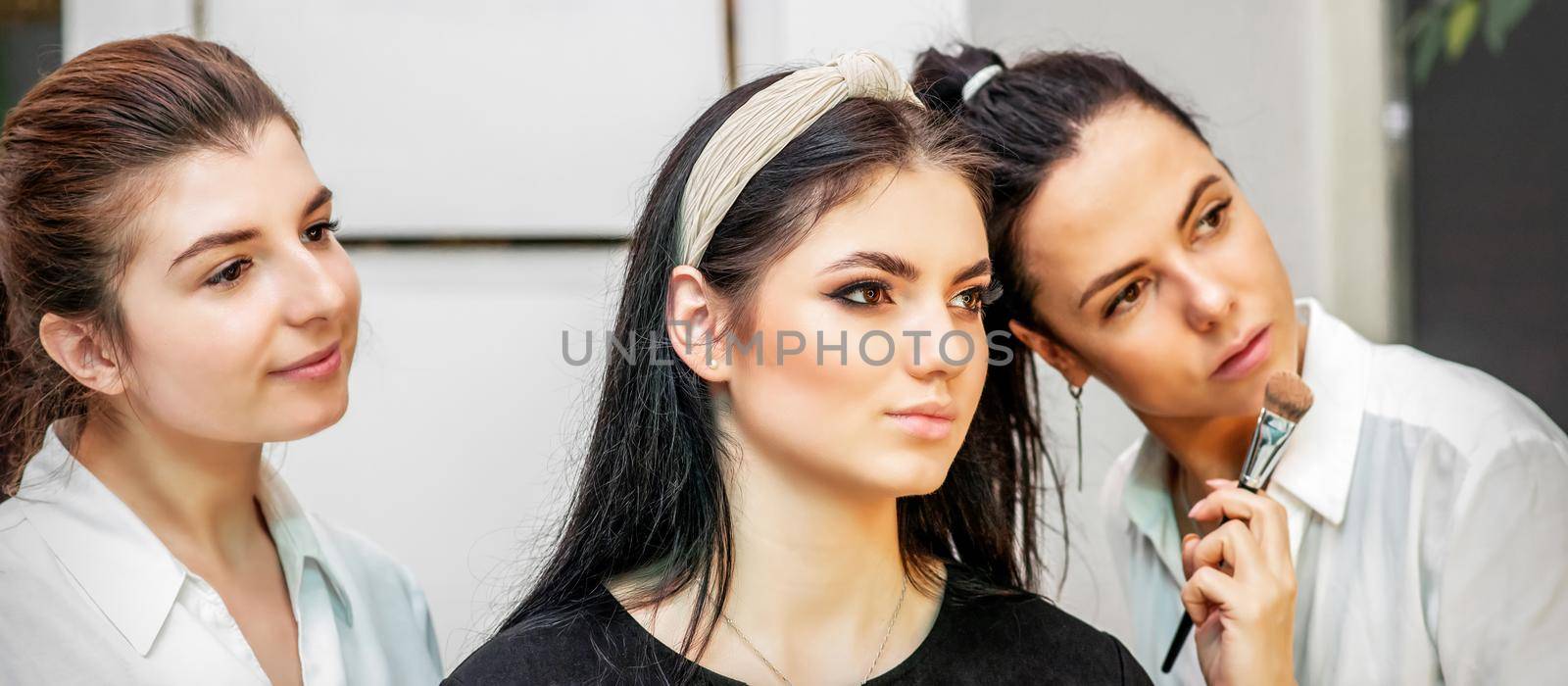 Make-up artist doing makeup for young beautiful bride applying wedding makeup in a beauty salon. by okskukuruza