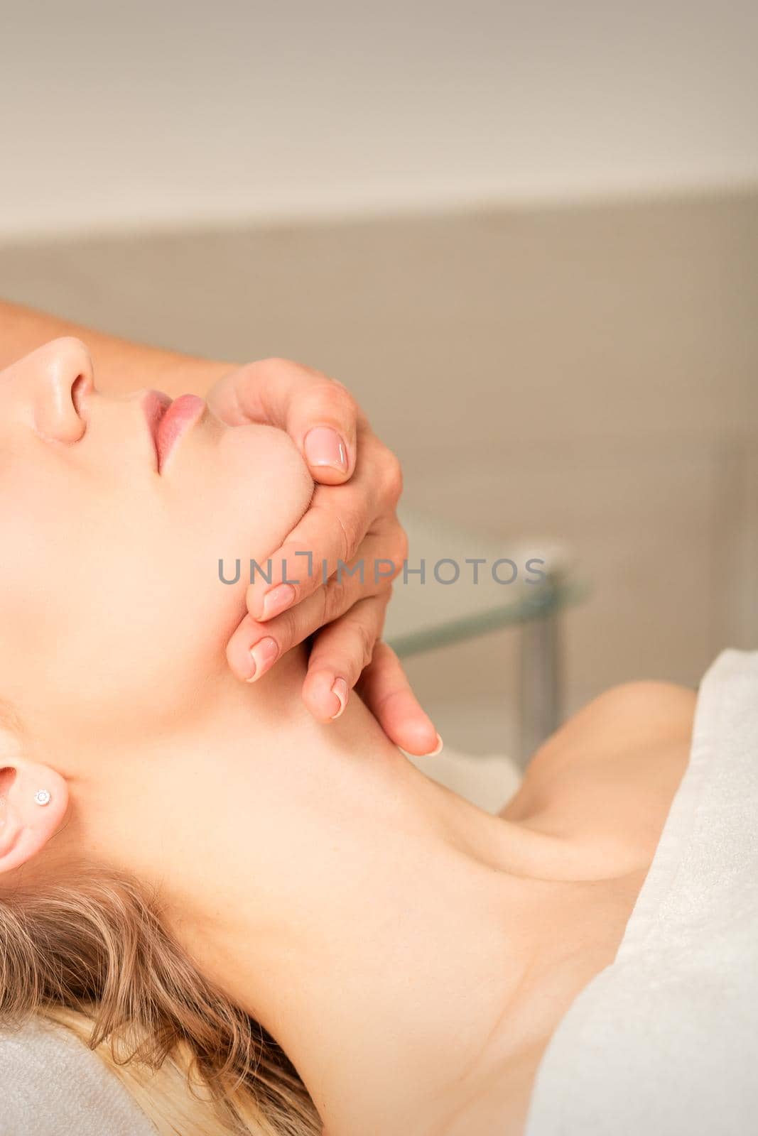 Cosmetologist hands doing facial massage on forehead and chin of young female at spa salon