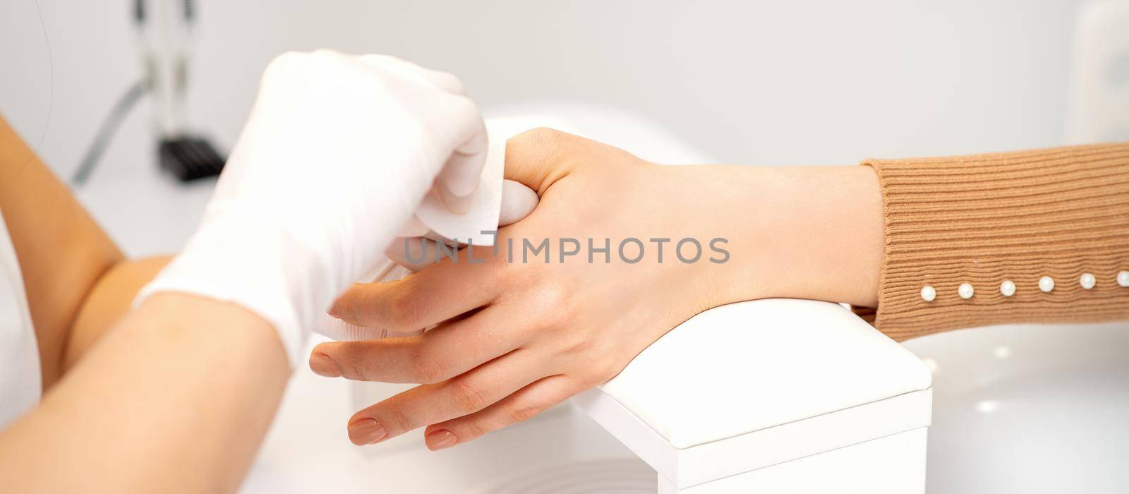 Hands of a manicurist in white protective gloves wipe female nails with a paper napkin in the salon