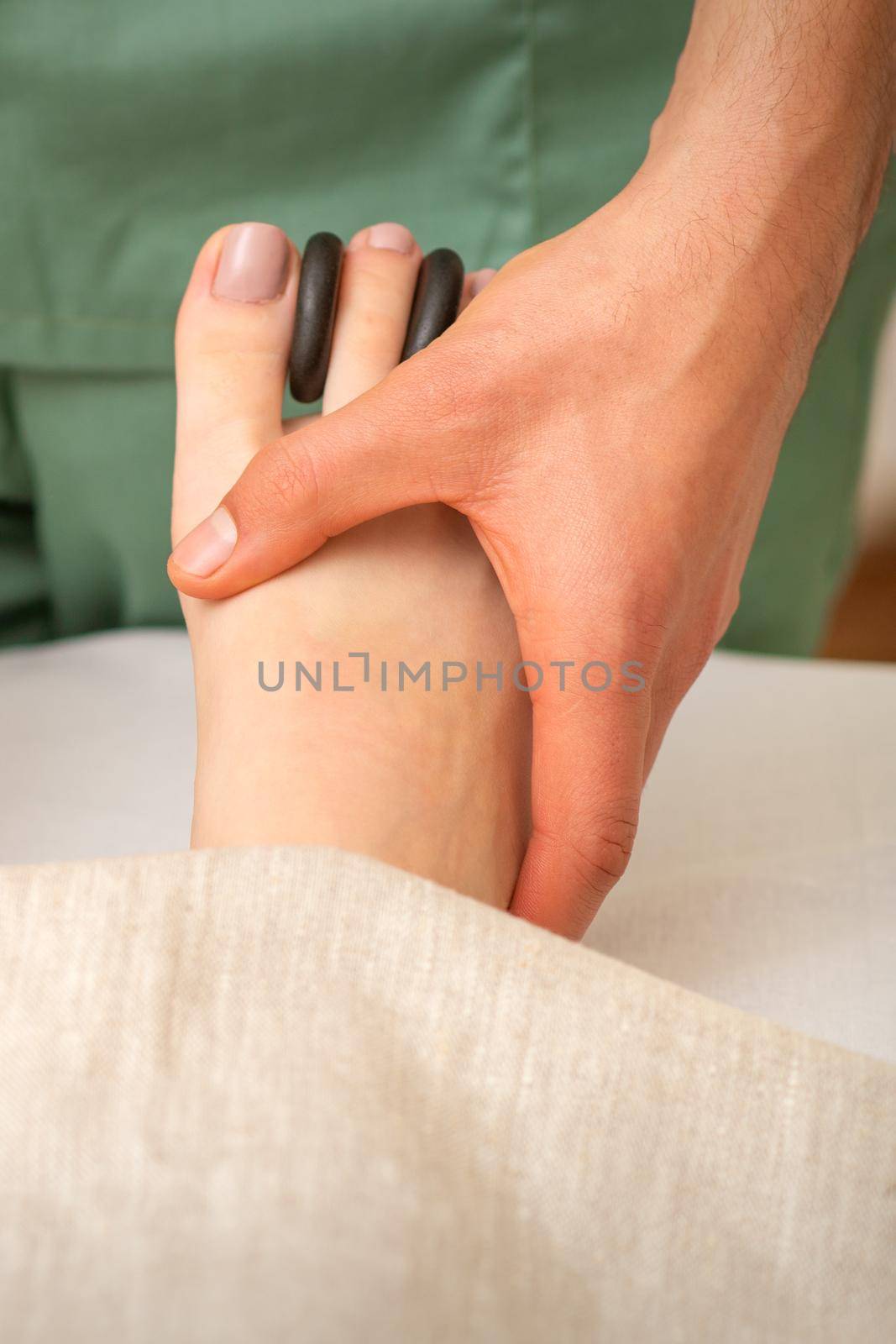 Massager doing feet and toes massage with rocks between a female toes. by okskukuruza