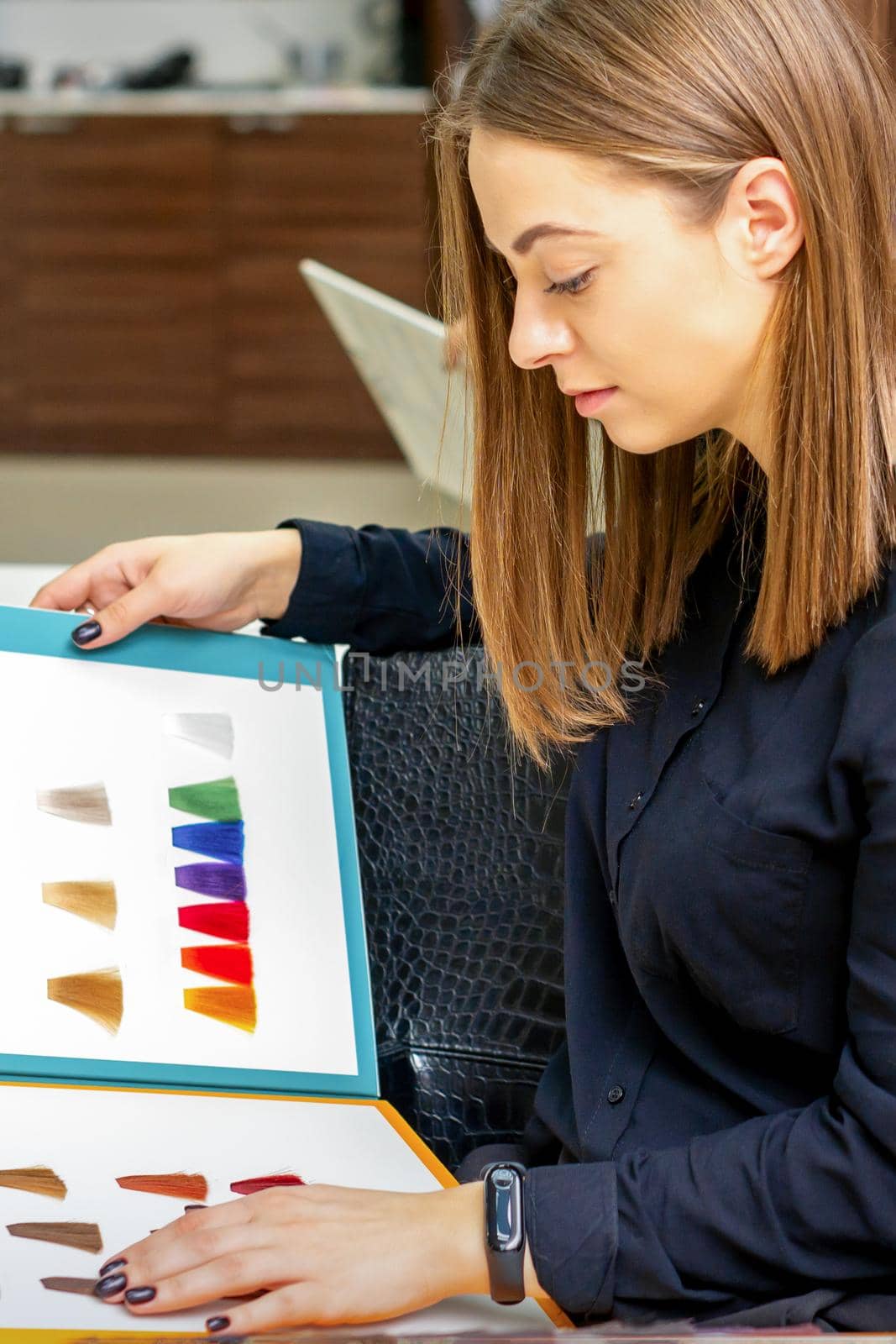 Young caucasian woman choosing a color from the hair color chart in a beauty salon. by okskukuruza