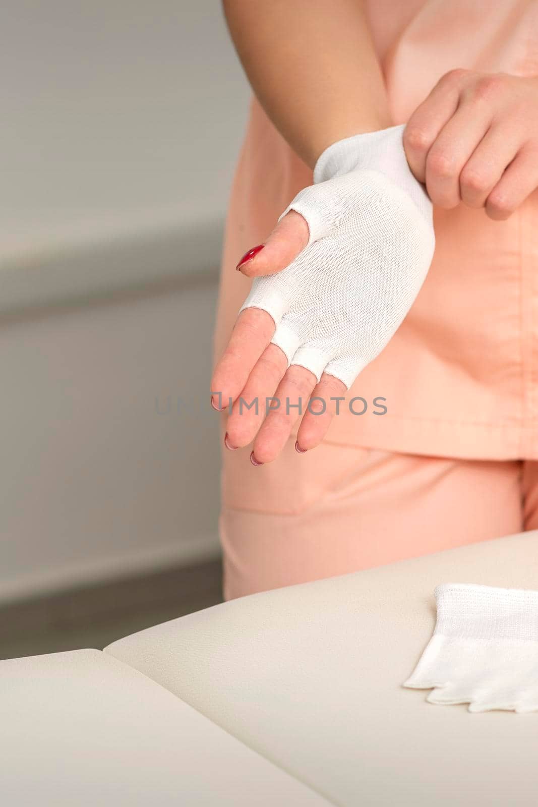 Cosmetologist in workwear wearing white bamboo fingerless gloves on her hands. by okskukuruza