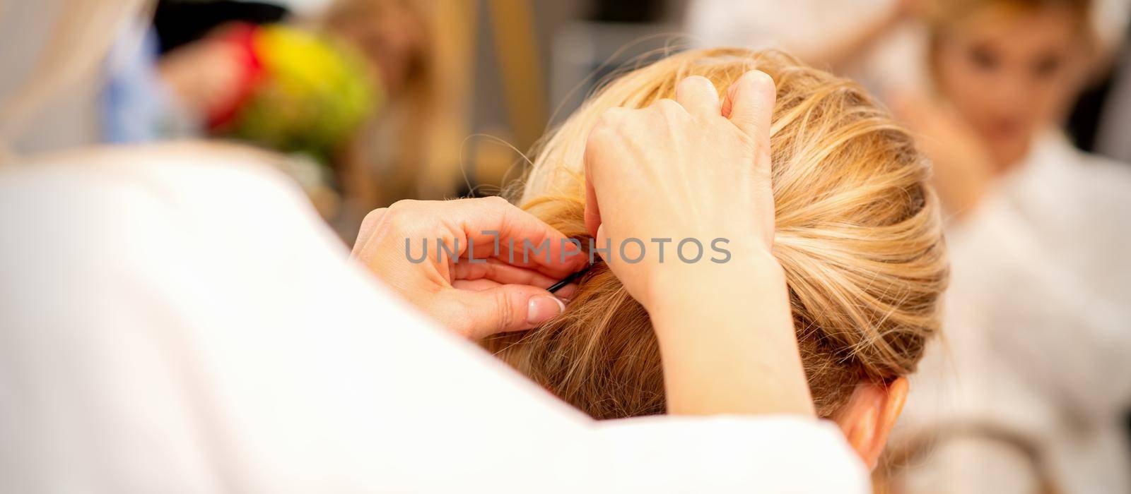 Hair stylist's hands doing professional hairstyling of female long hair in a beauty salon