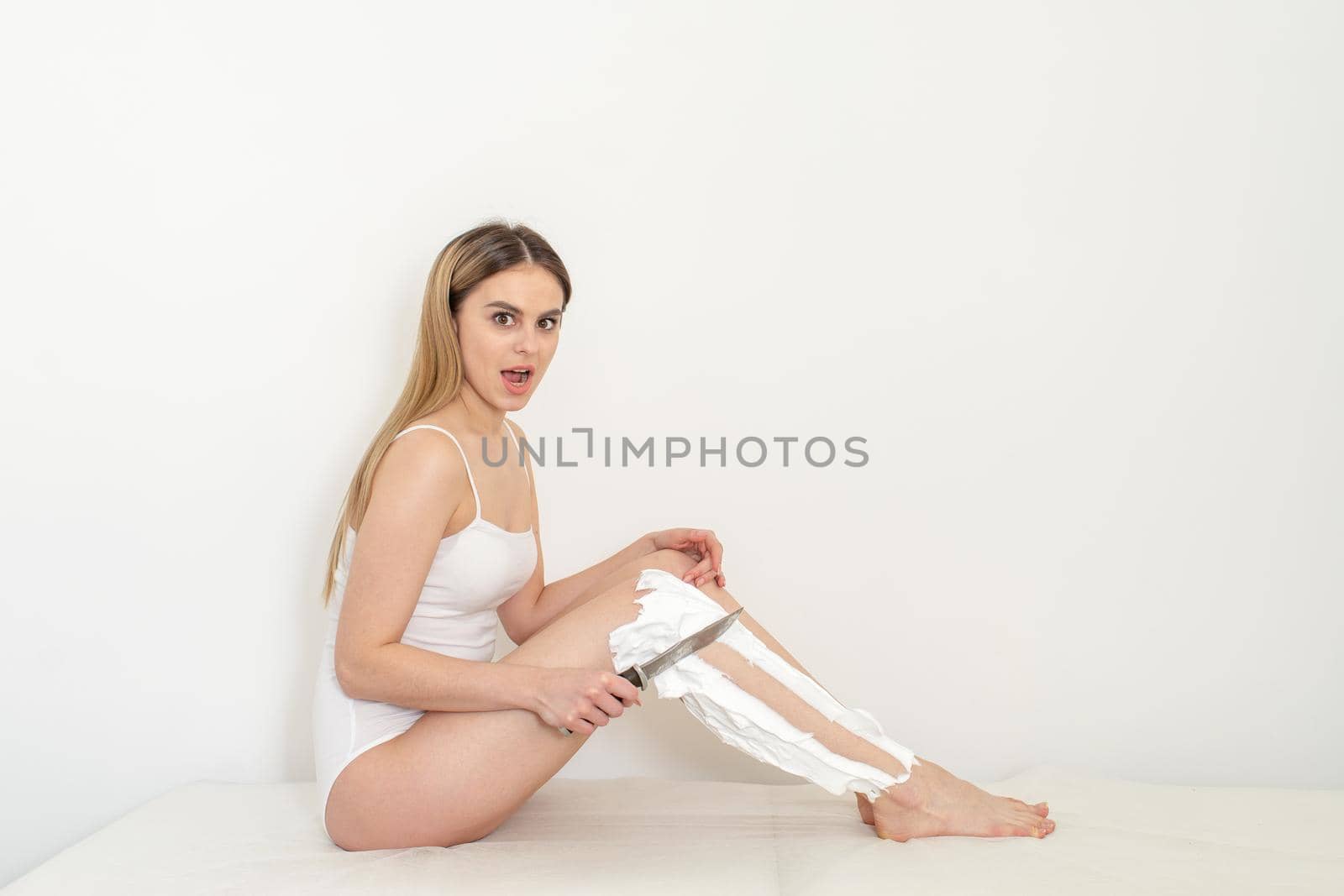 Beautiful caucasian woman shaving her legs with a knife with shaving foam on white background. Depilation and epilation concept