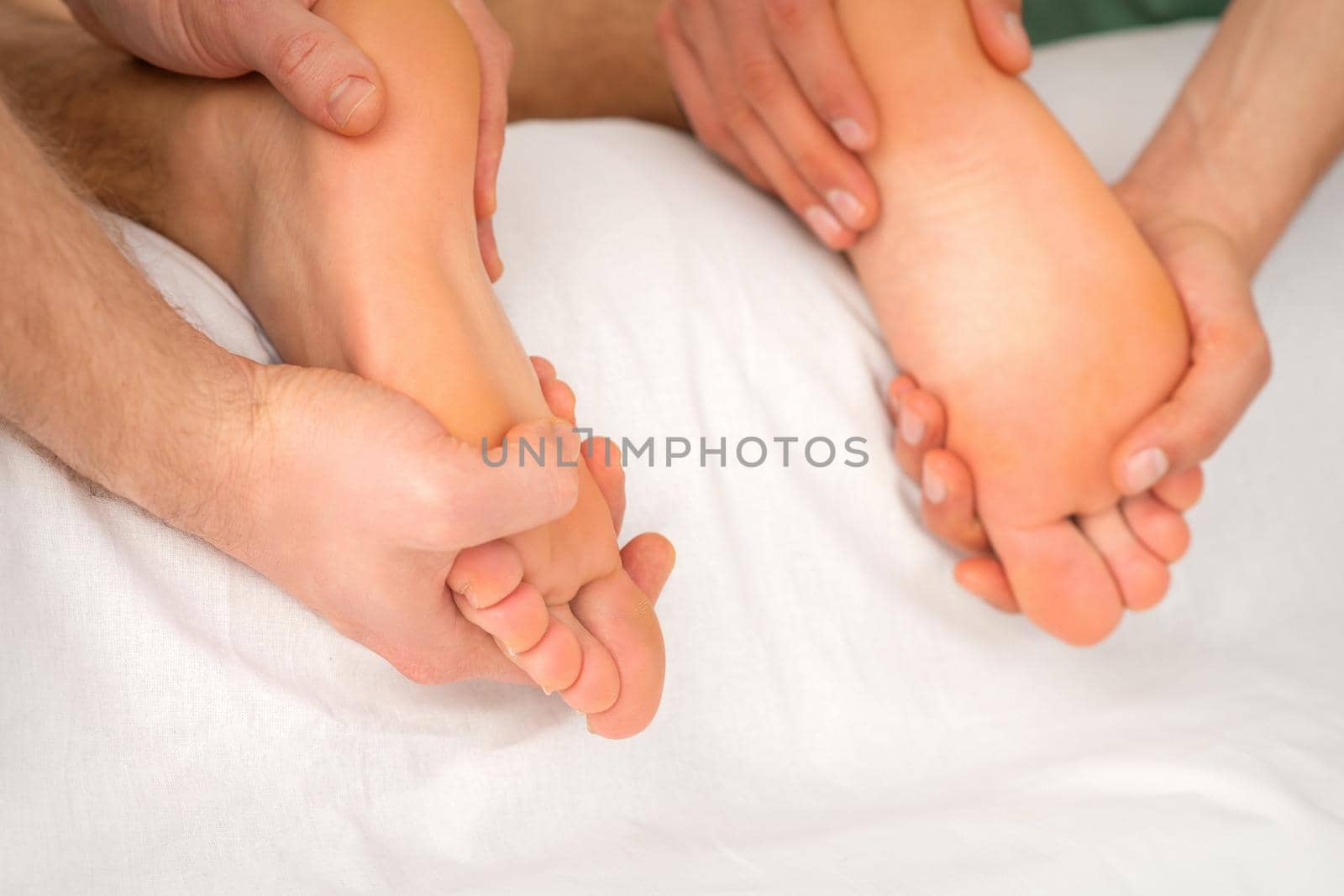 Relaxing double massage on the female feet by two masseurs in spa salon