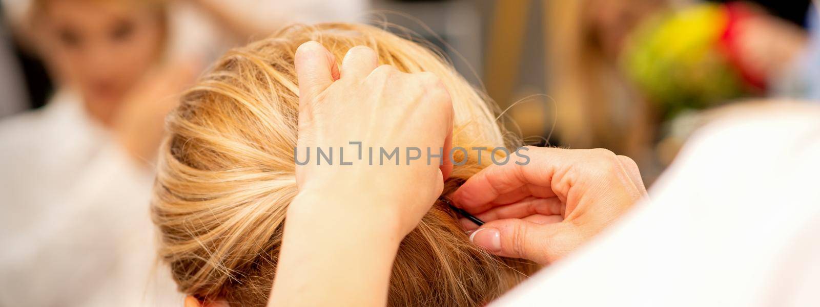 Hair stylist's hands doing professional hairstyling of female long hair in a beauty salon. by okskukuruza