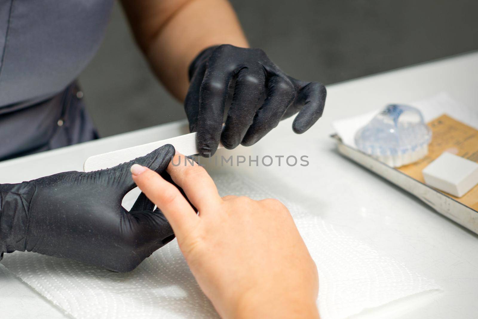 Woman receiving a manicure with nail file by a manicure master in a nail salon
