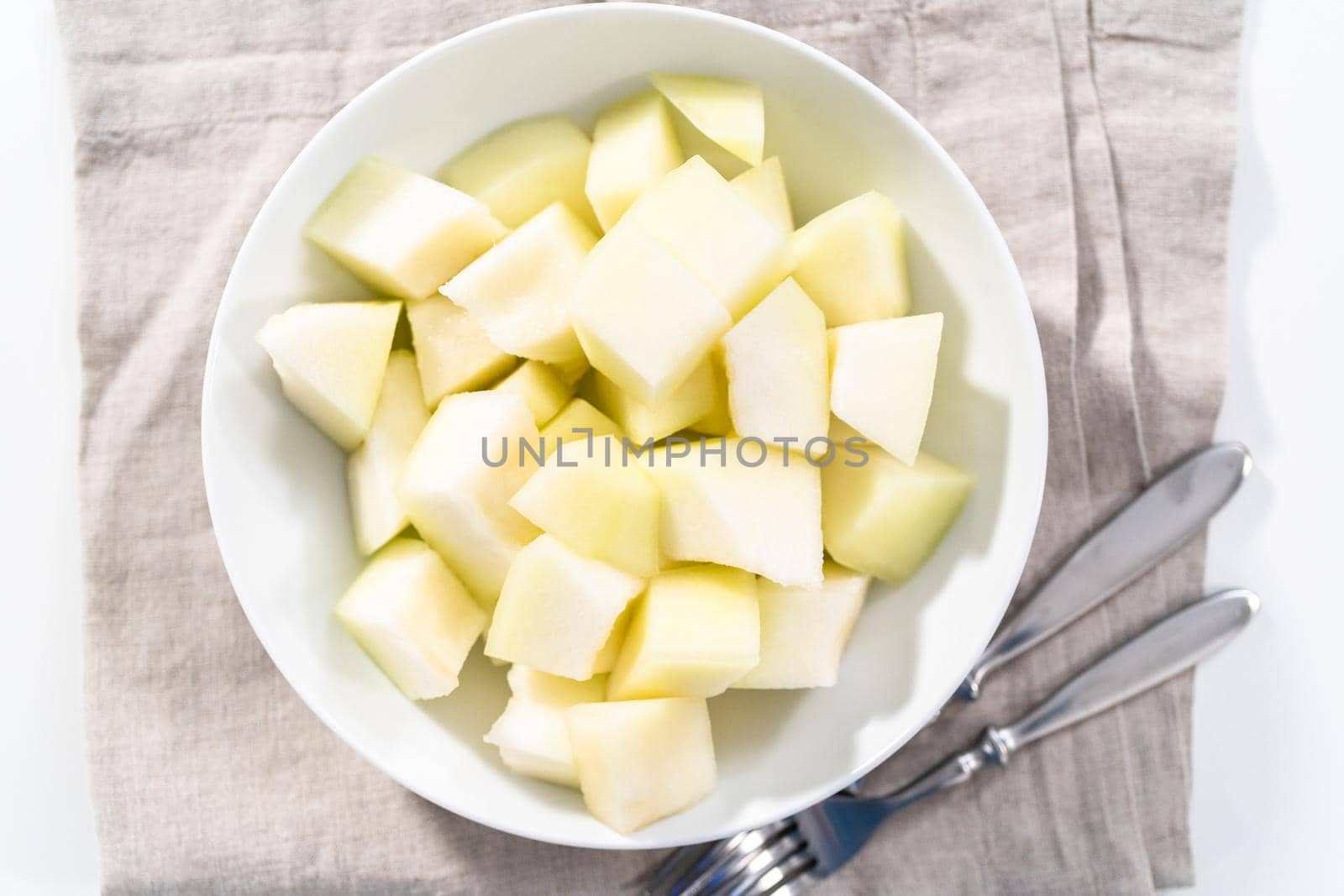 Sliced golden dewlicious melon in a white bowl.