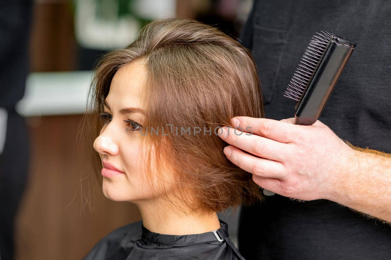 Male hairdresser works on the hairstyle of the young caucasian brunette woman at a hair salon