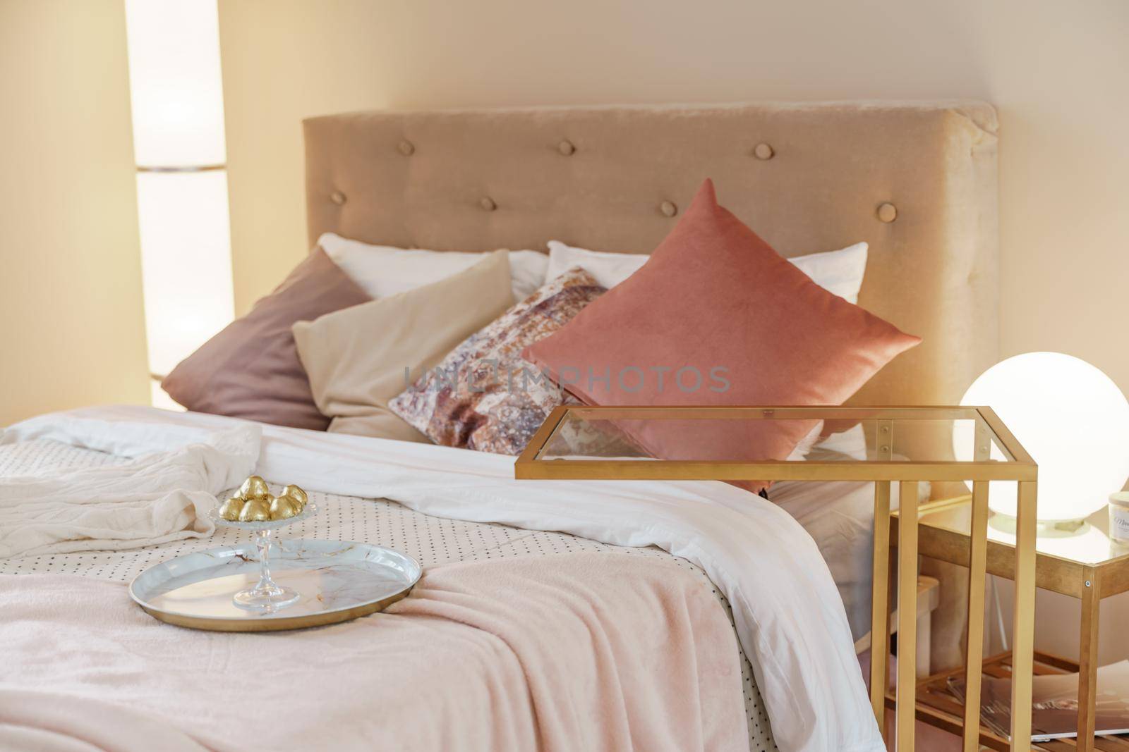 Bedroom interior in light colors with wooden furniture and pillows. Lamps on both sides