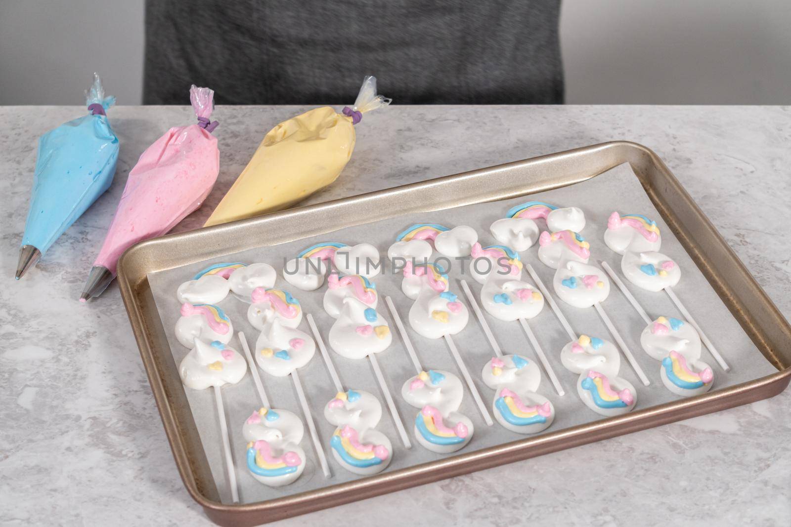 Unbaked unicorn theme meringue pops on a baking sheet lined with parchment paper.