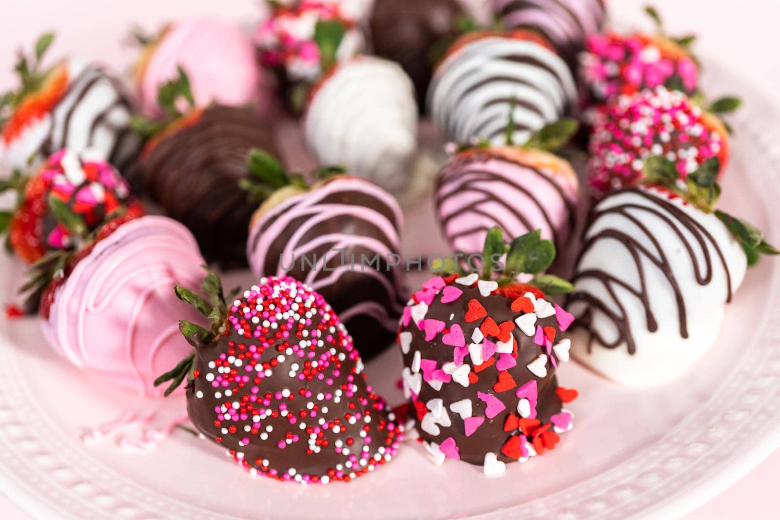 Variety of chocolate dipped strawberries on a pink cake stand.